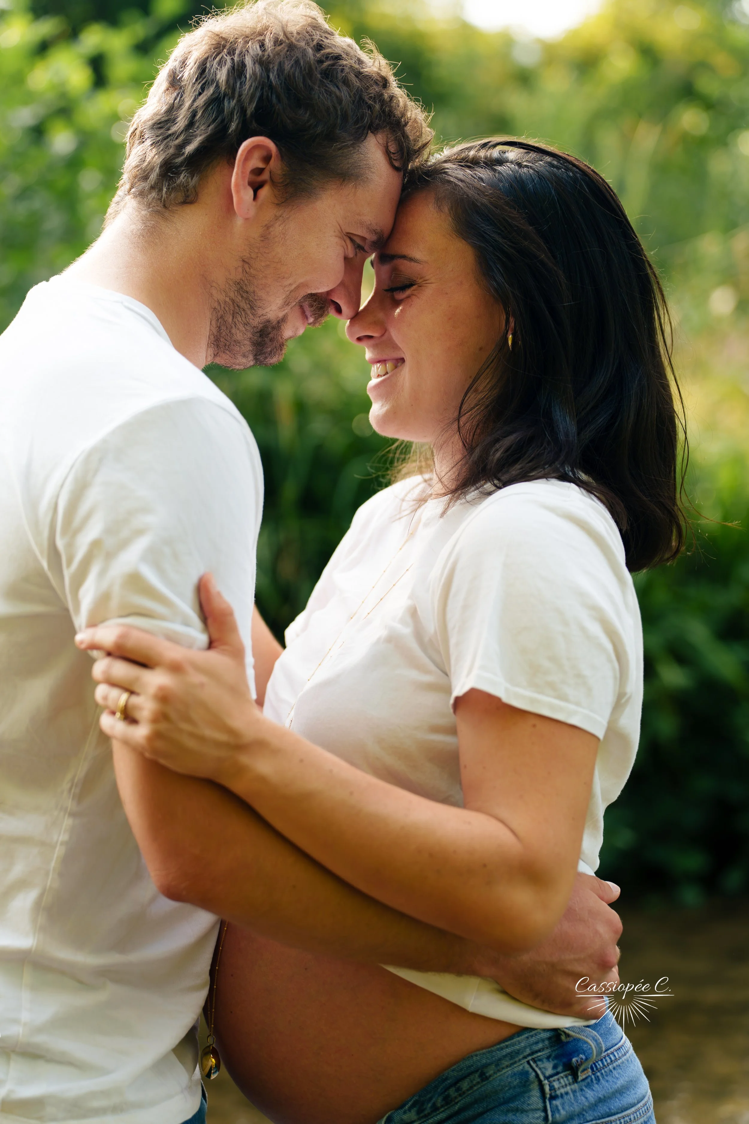 Un couple s'apprête à s'embrasser tendrement, la tête contre la tête, dans un cadre extérieur verdoyant et lumineux.