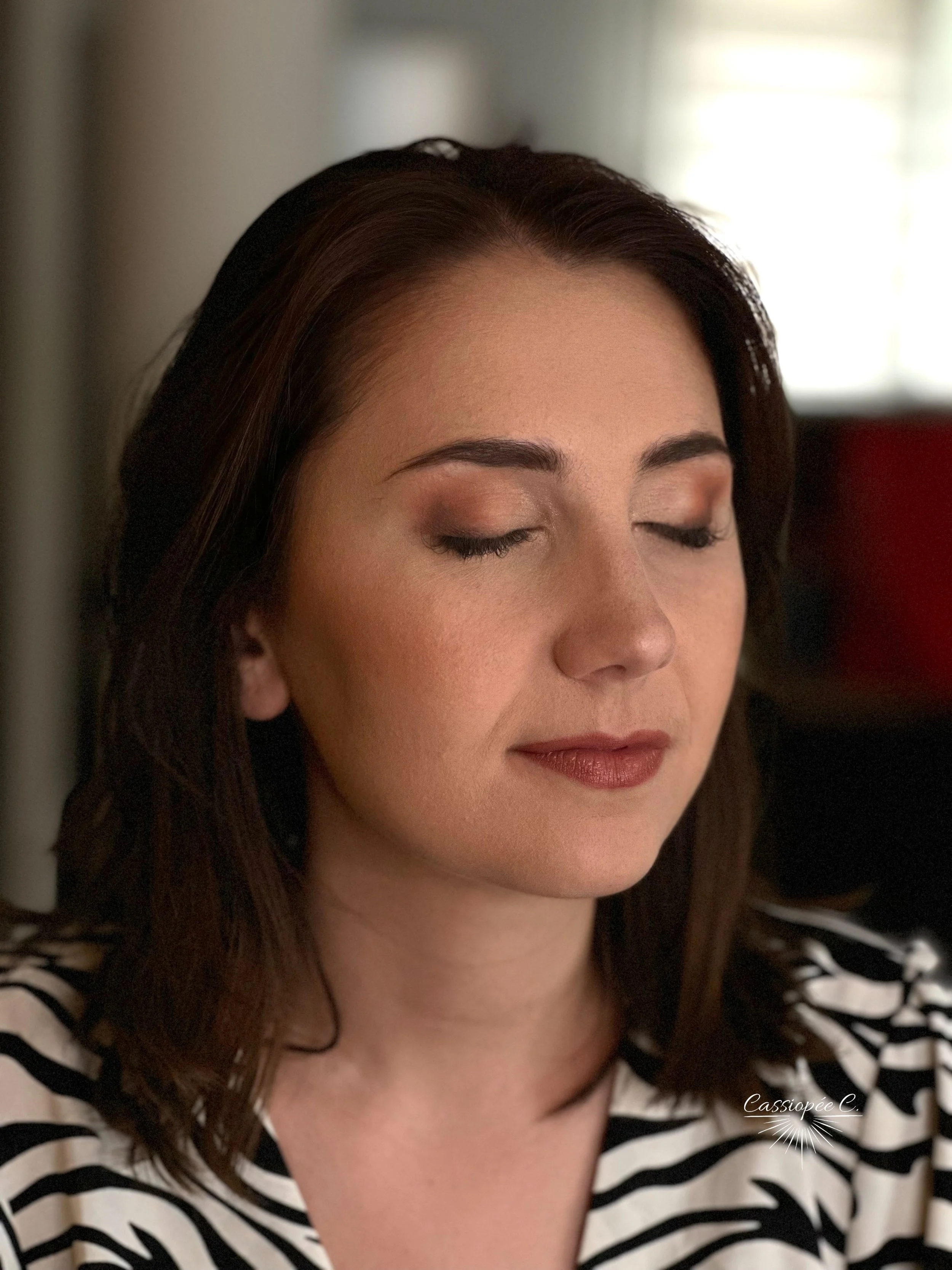 Une femme aux yeux fermés avec des cheveux marron foncé, avec un beau maquillage d'invitée pour un mariage.