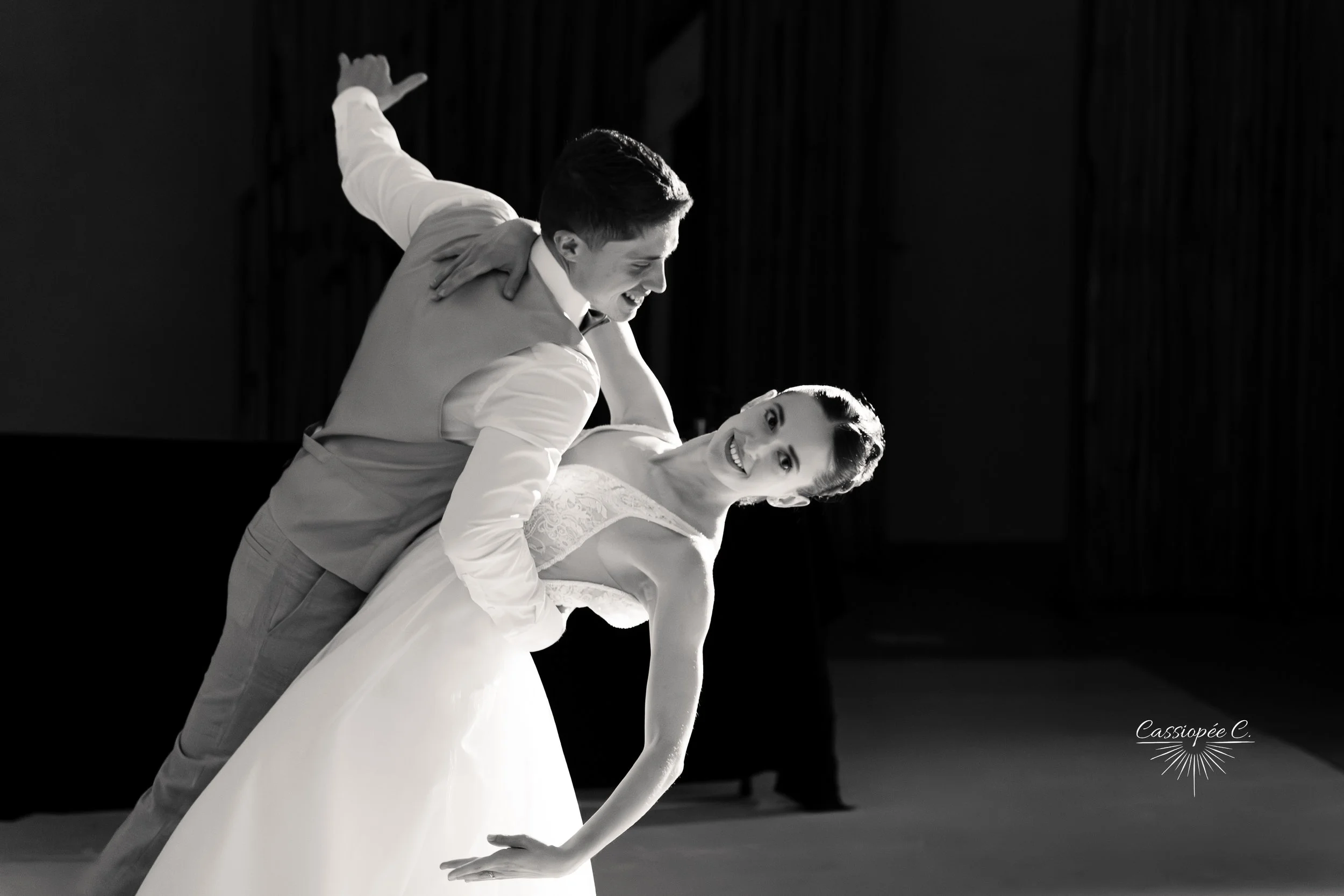 Un couple de danseurs en tenue de mariage effectue une danse lors d'une performance, avec le marié inclinant la mariée en arrière, dans une scène en noir et blanc.