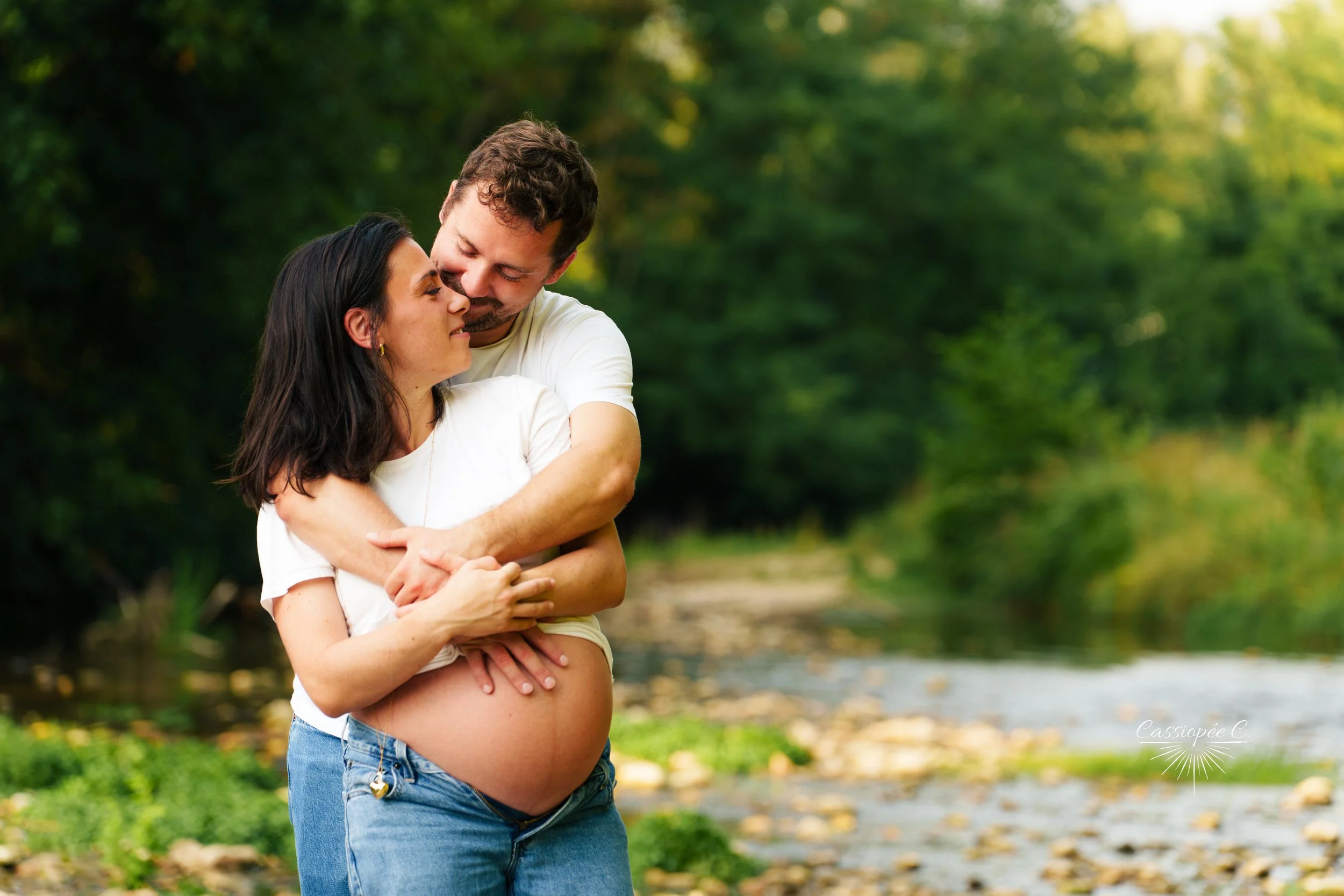 Femme enceinte et homme s'embrassant dans un parc vert lors d'une journée ensoleillée.