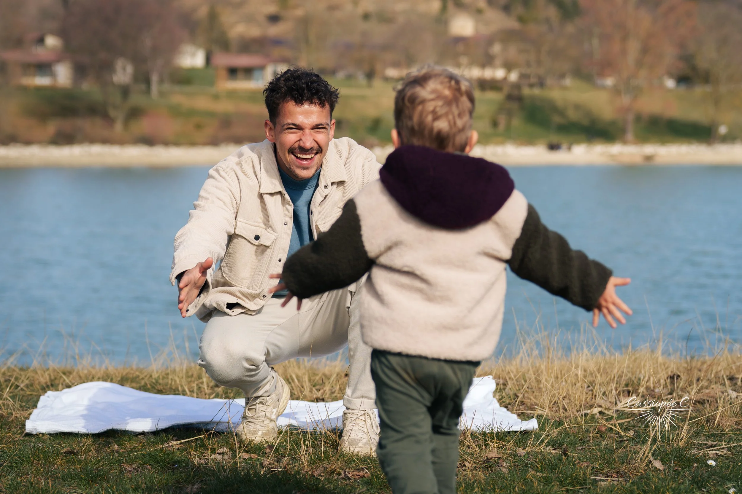 Le papa joue avec son enfant près d'un lac en plein air, l'homme sourit en regardant l'enfant, lors d'une journée ensoleillée avec un paysage de nature en arrière-plan.