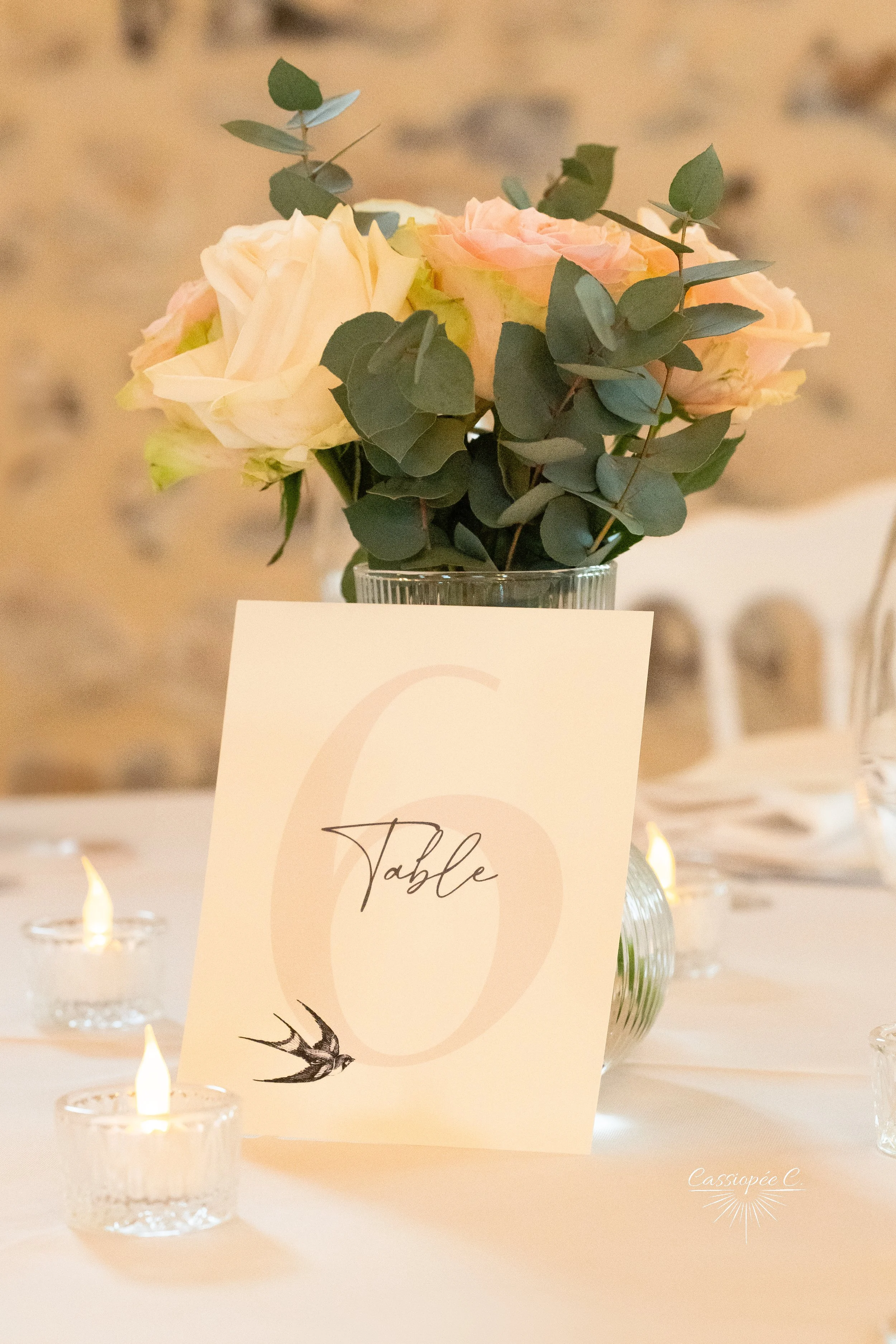 Centre de table avec bouquet de roses et eucalyptus, carte indiquant la table 6, bougies allumées, ambiance élégante