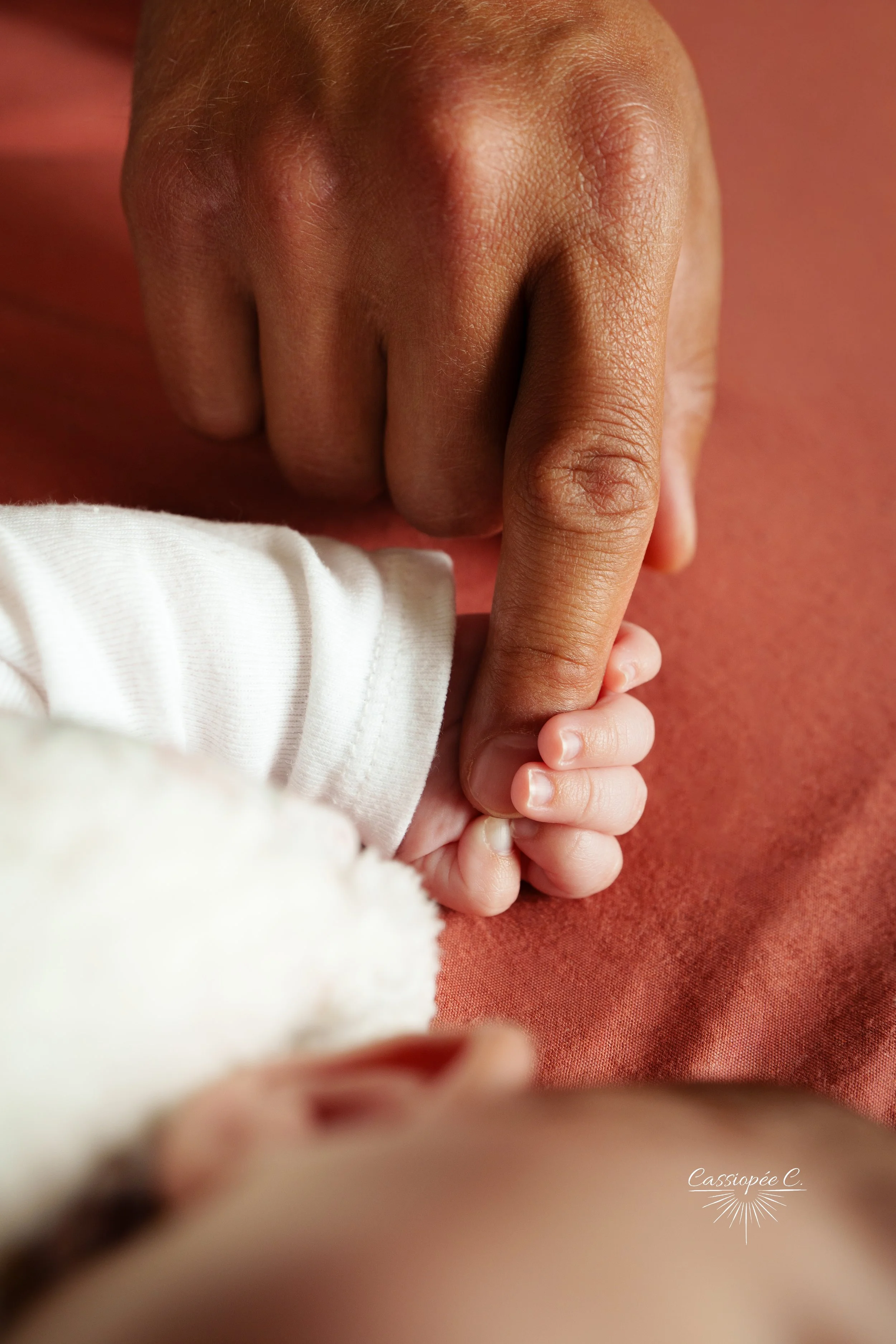 Un bébé tient le doigt d'un adulte, ils sont proches et montrent une connexion affectueuse.