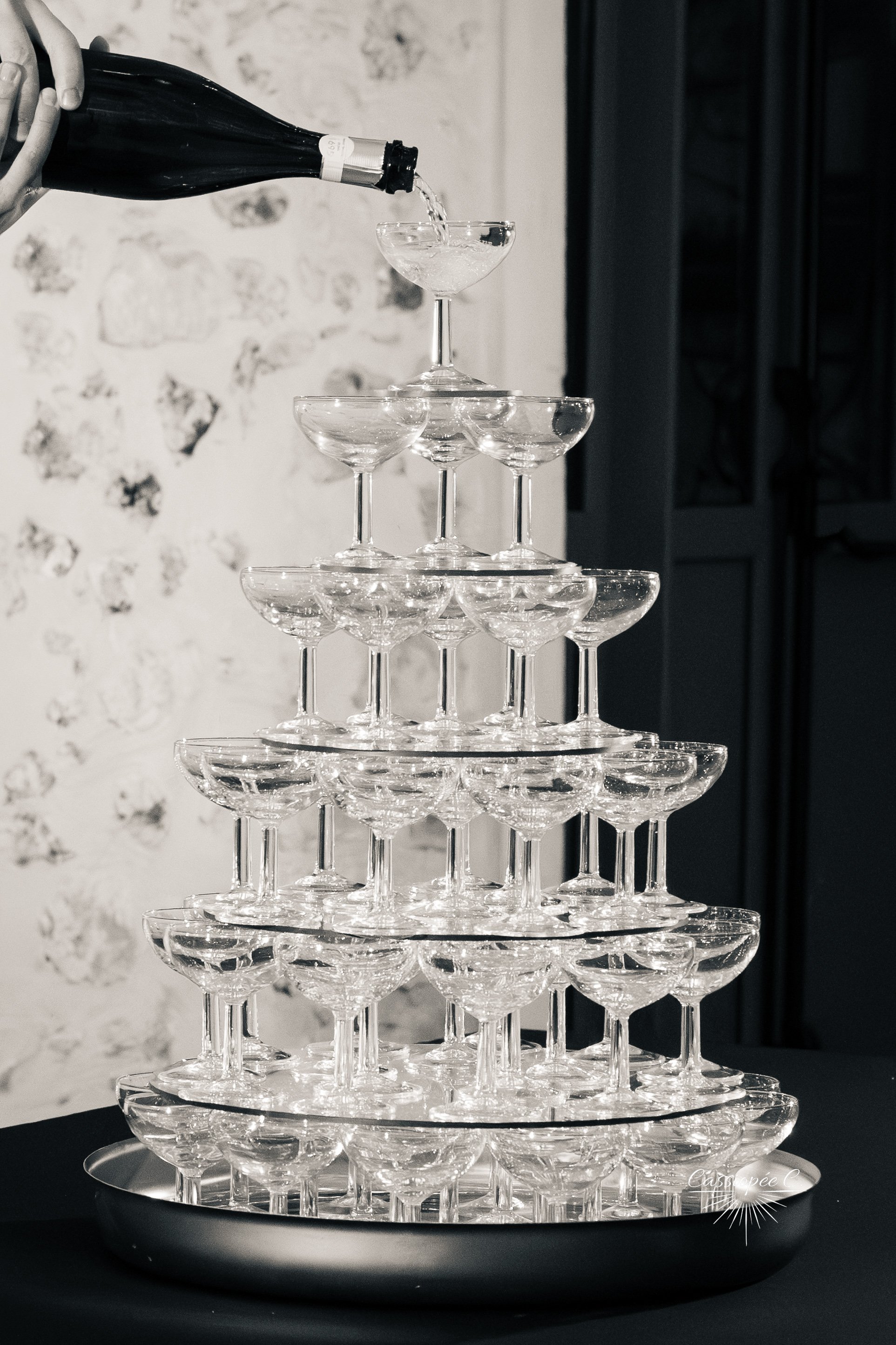 Une pyramide de verres à cocktail en verre transparent avec une bouteille de champagne versée dans le verre supérieur.