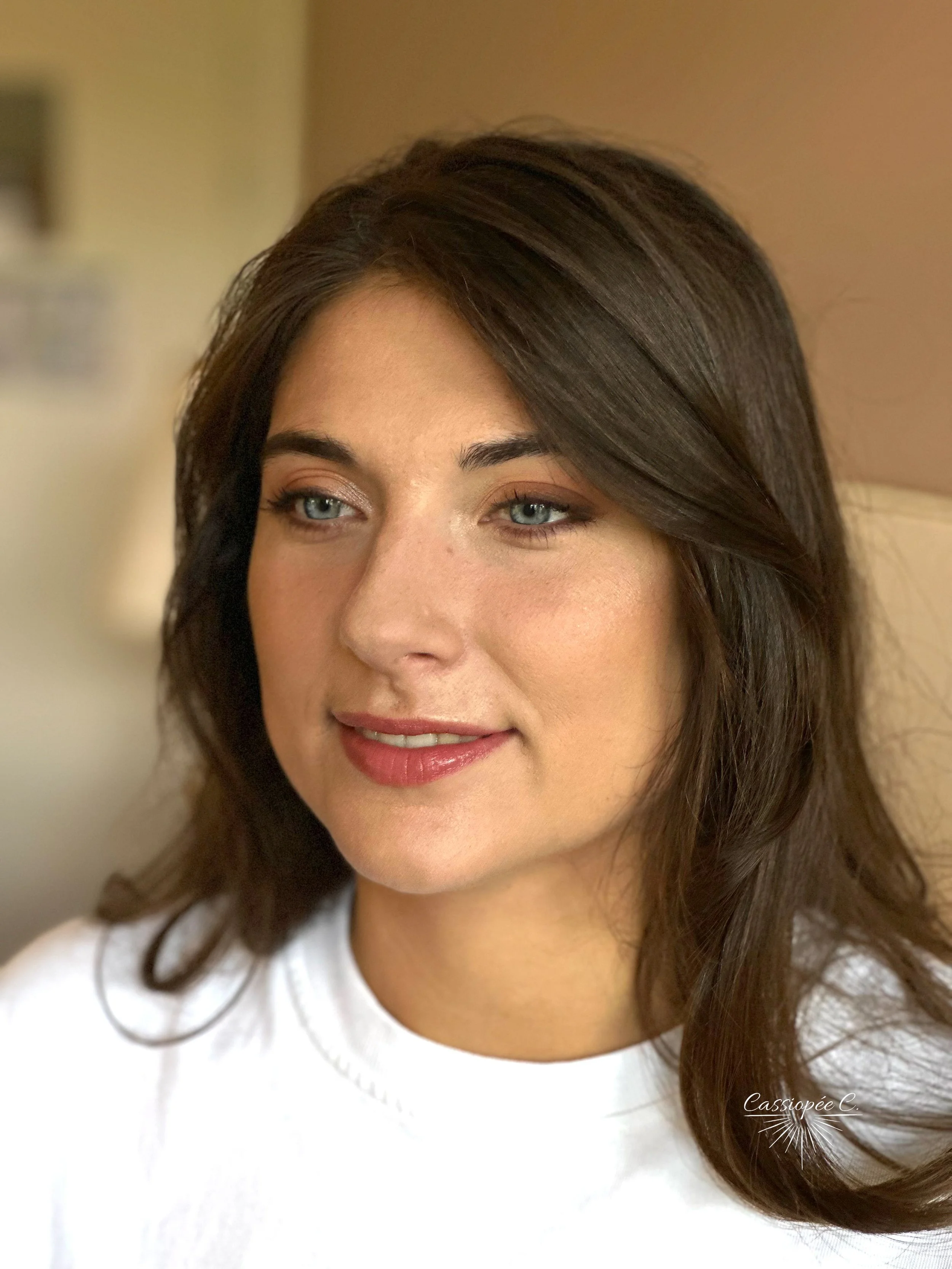 Un portrait d'une femme aux yeux fermés, avec des cheveux longs, bruns et ondulés, portant un t-shirt blanc, maquillage pour un mariage.