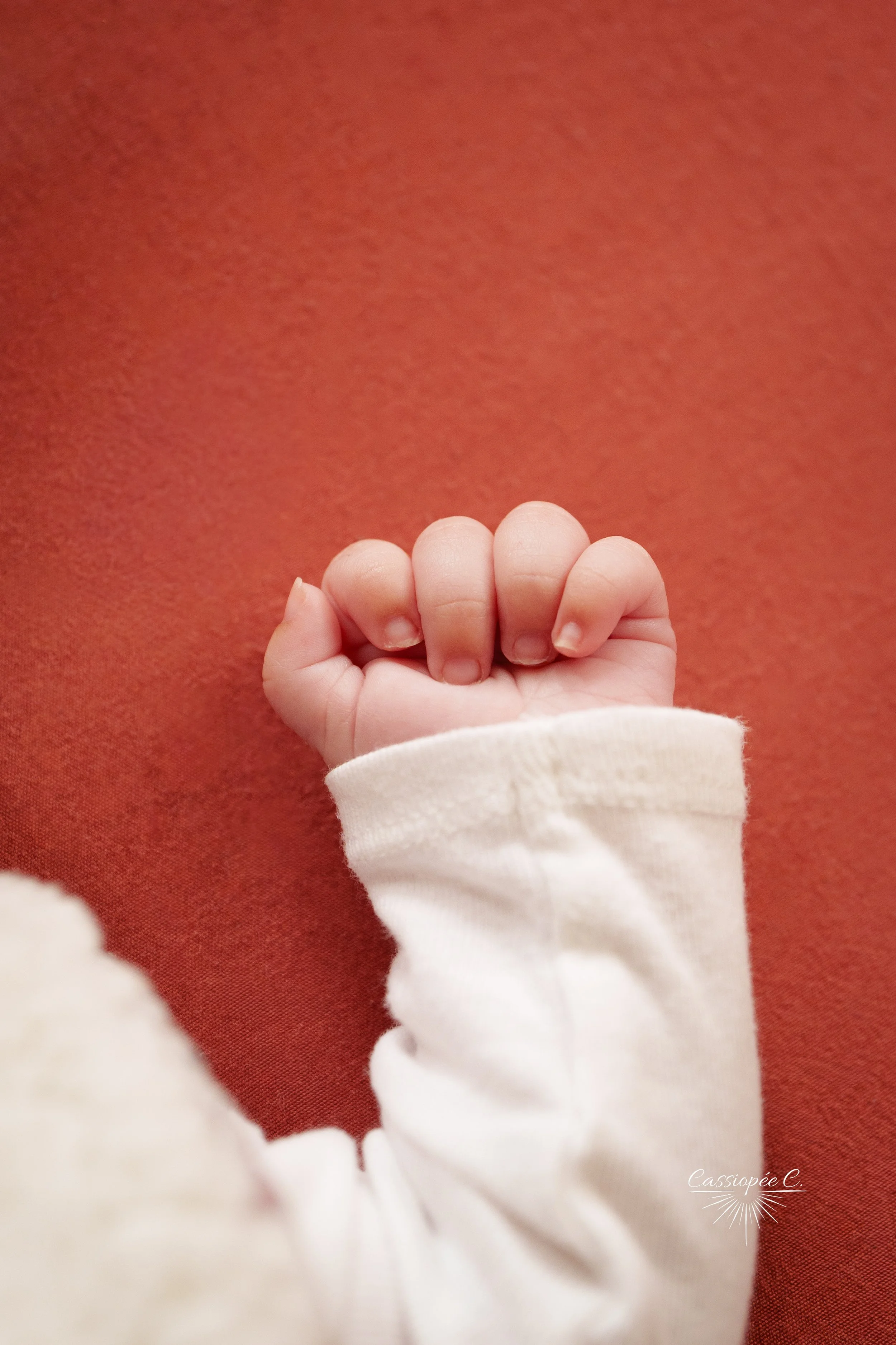 Main d'un bébé avec un vêtement blanc, contre un fond rouge