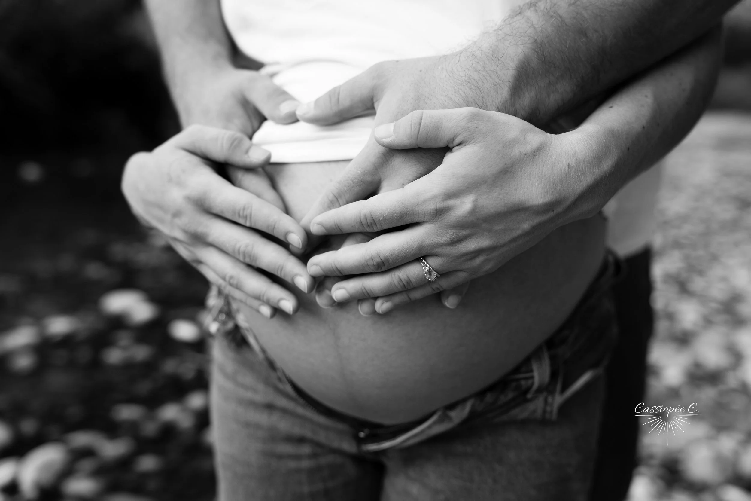 Deux mains joignent une autre main posée sur le ventre d'une femme enceinte, en noir et blanc.