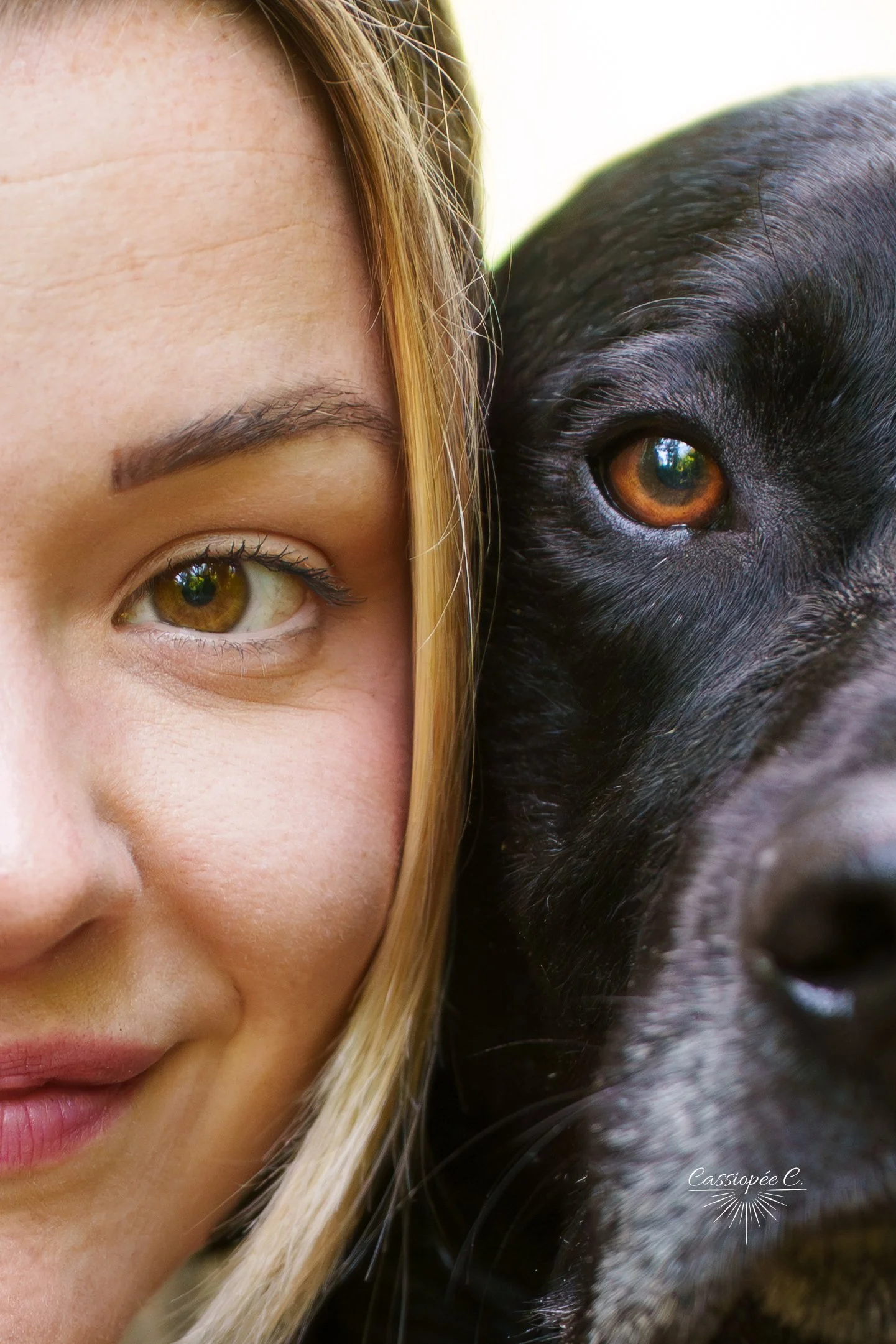 Un gros plan sur le visage d'une femme avec un œil marron. À côté d'elle, une tête de chien noir, montrant un œil marron et un pelage noir et gris.