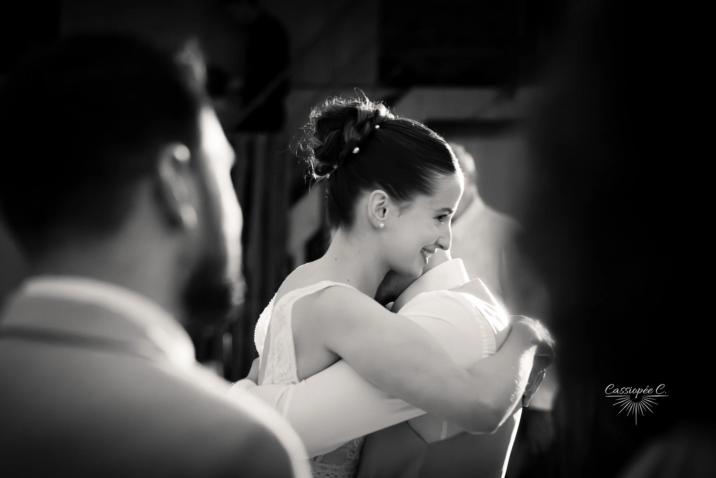 Une femme en robe de mariée enlace son mari, photo en noir & blanc.