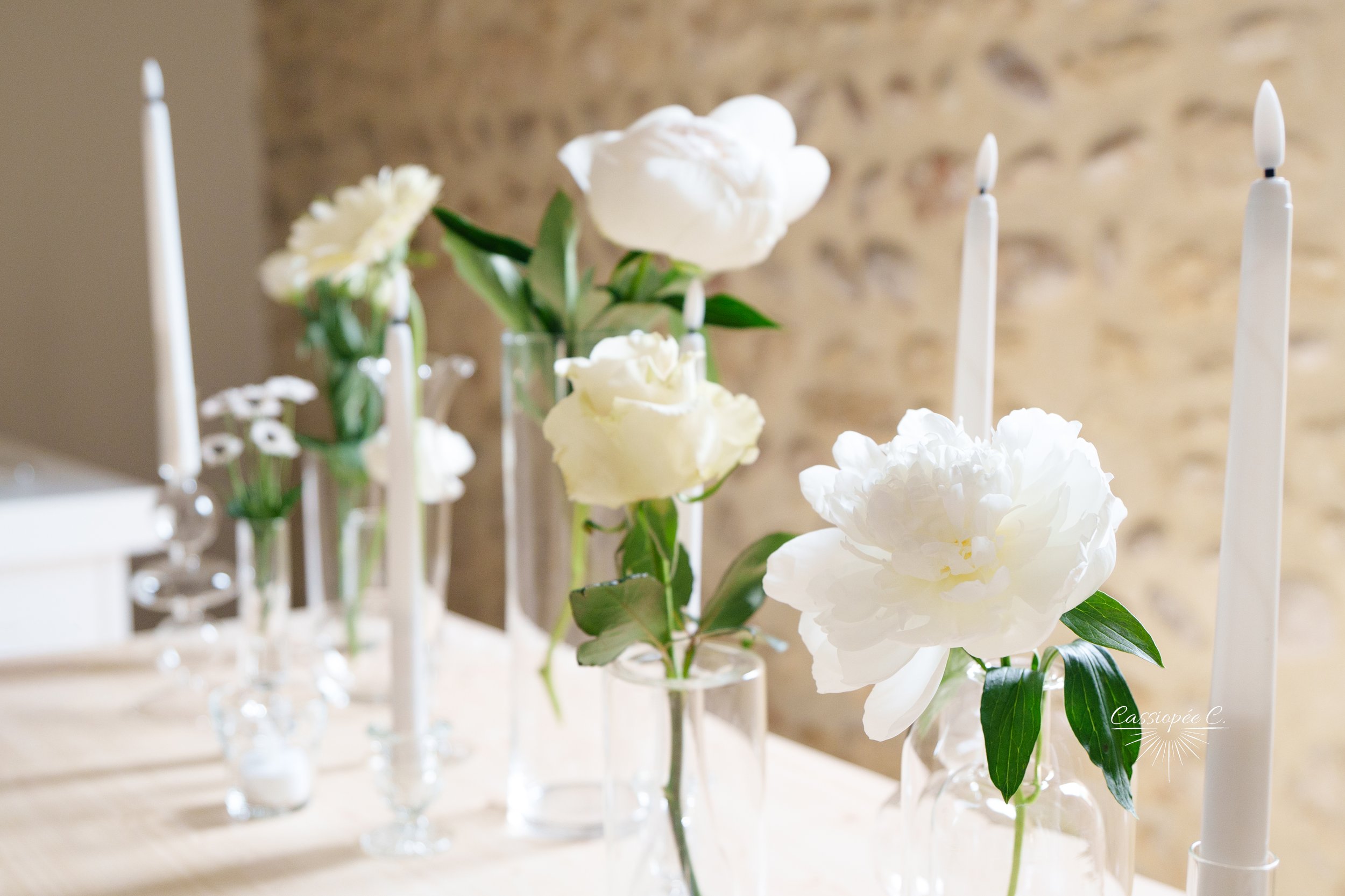 Vase avec des fleurs blanches, principalement des pivoines, et des bougies dans des chandeliers, décor d'intérieur élégant.