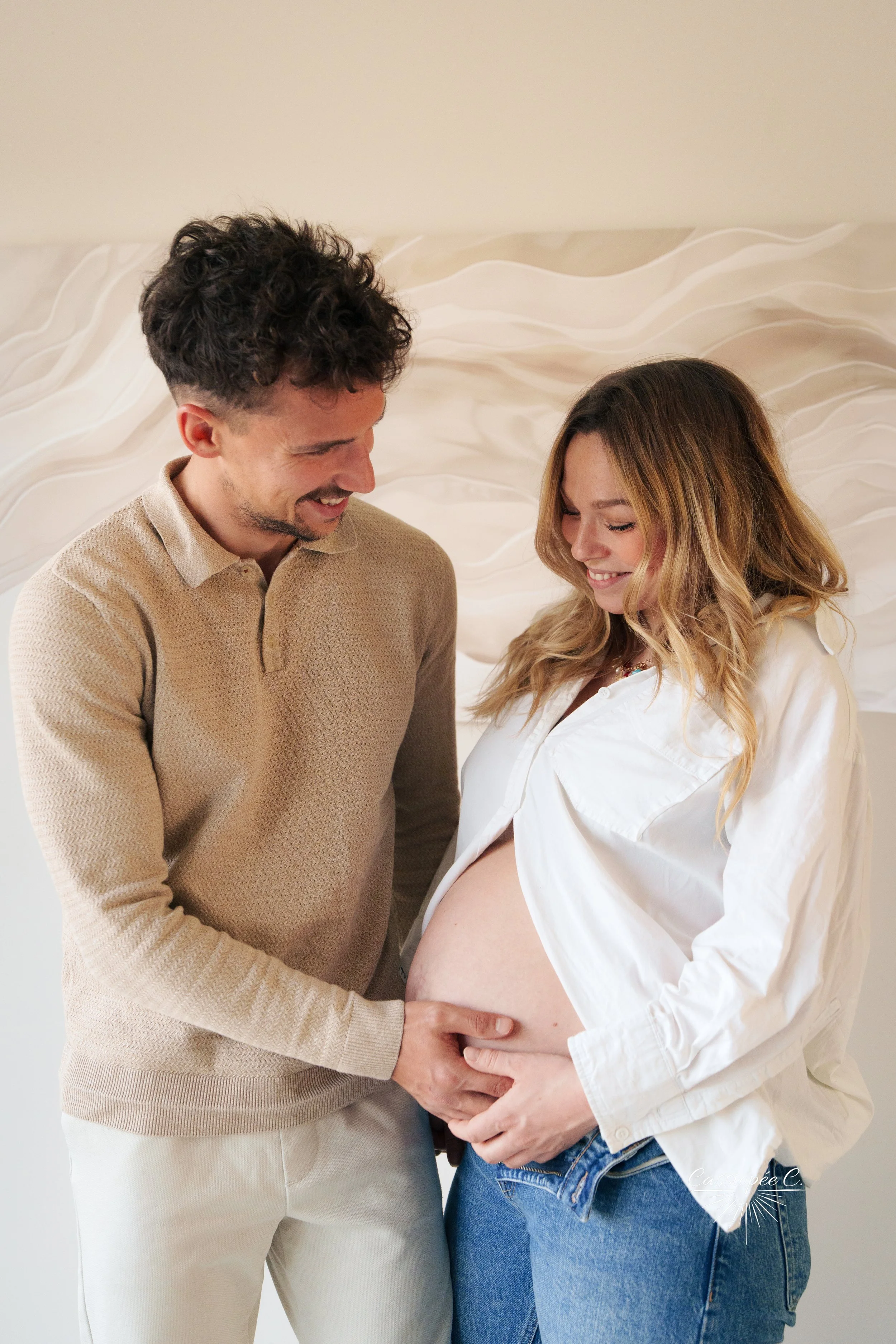 Un couple souriant, la femme enceinte, tenant son ventre avec la main tandis que l'homme repose la main sur son ventre.