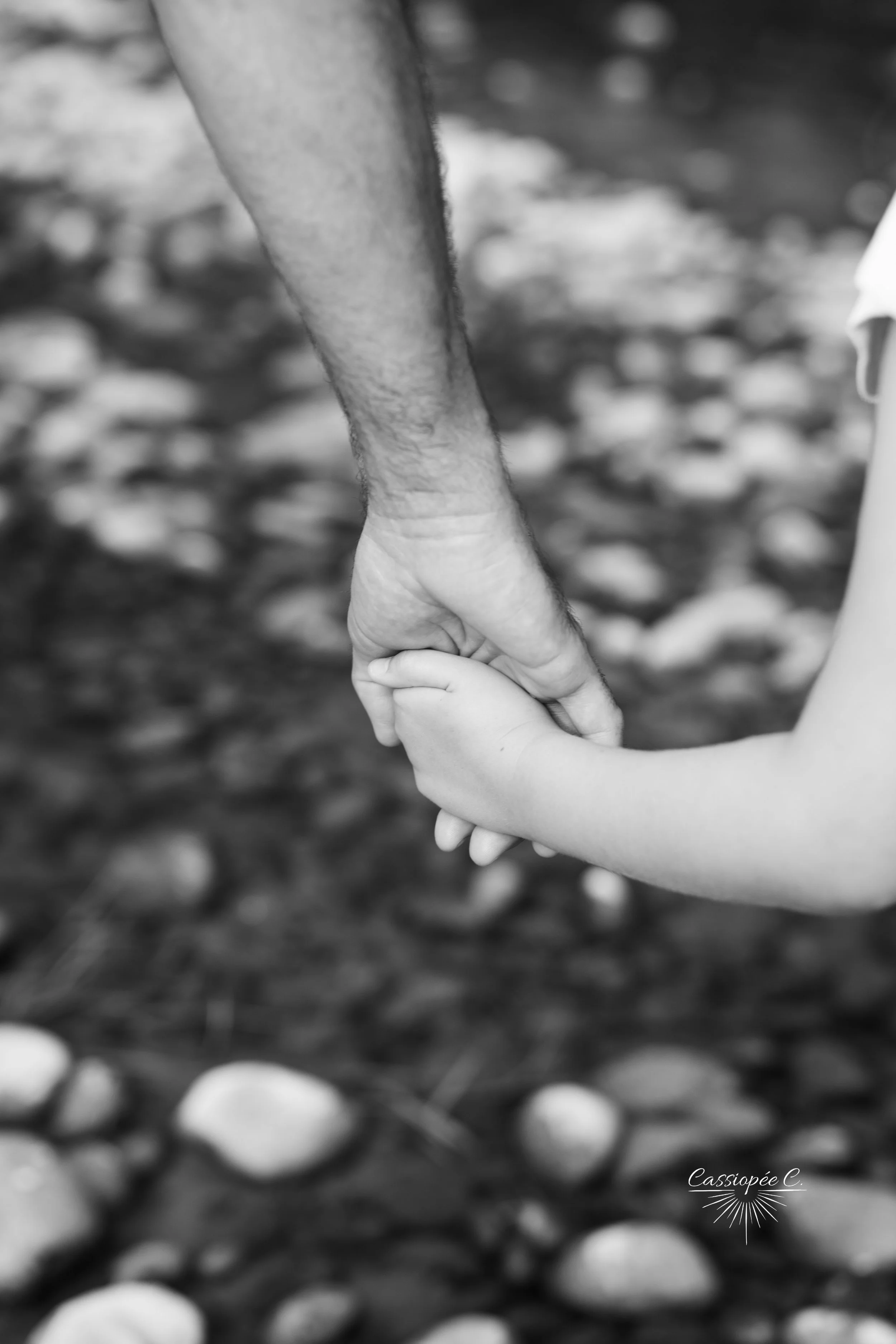 Une main d'adulte tient celle d'un enfant avec des cailloux en arrière-plan.