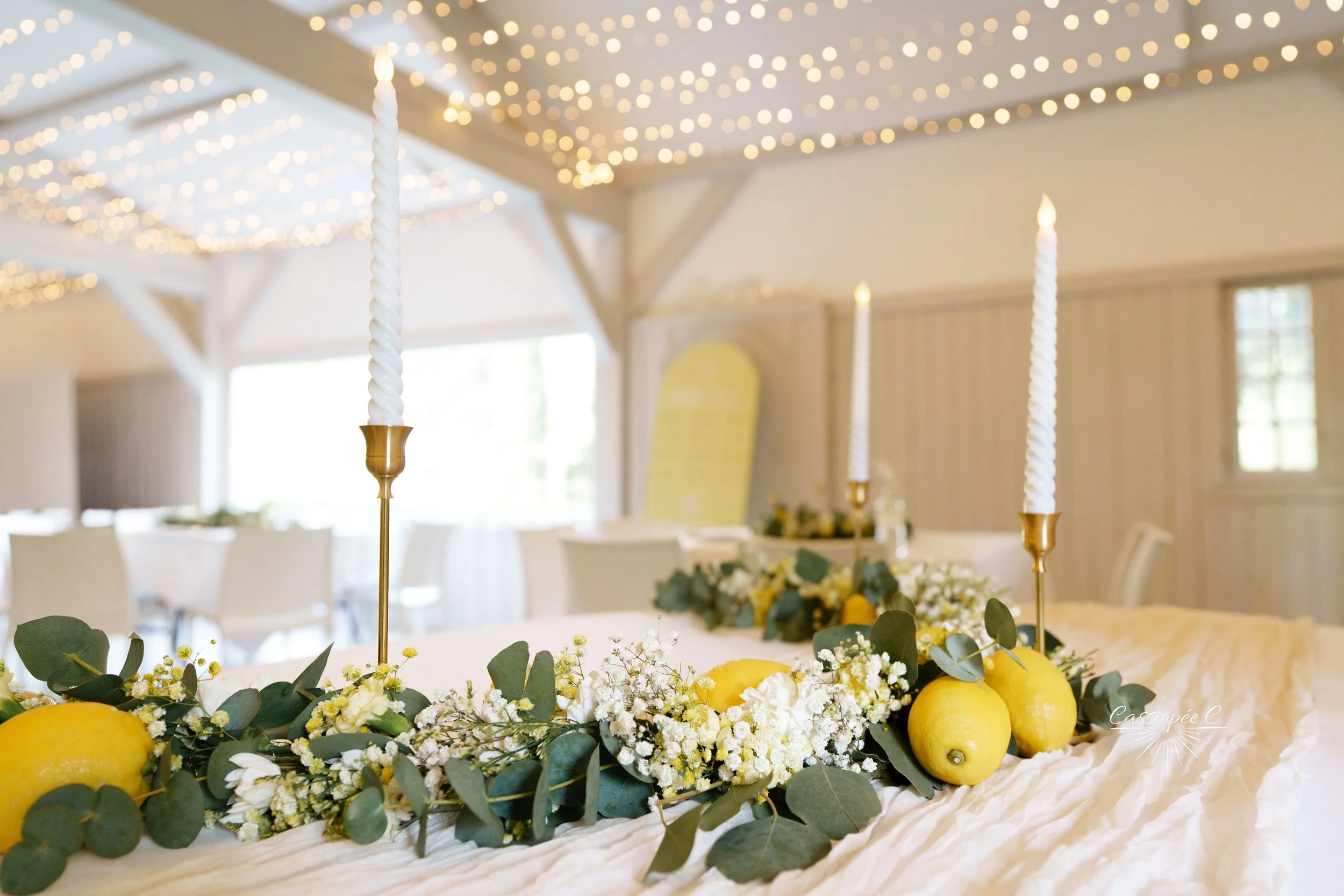 Décoration de table avec des citrons, des fleurs blanches et des bougies allumées dans un intérieur lumineux.