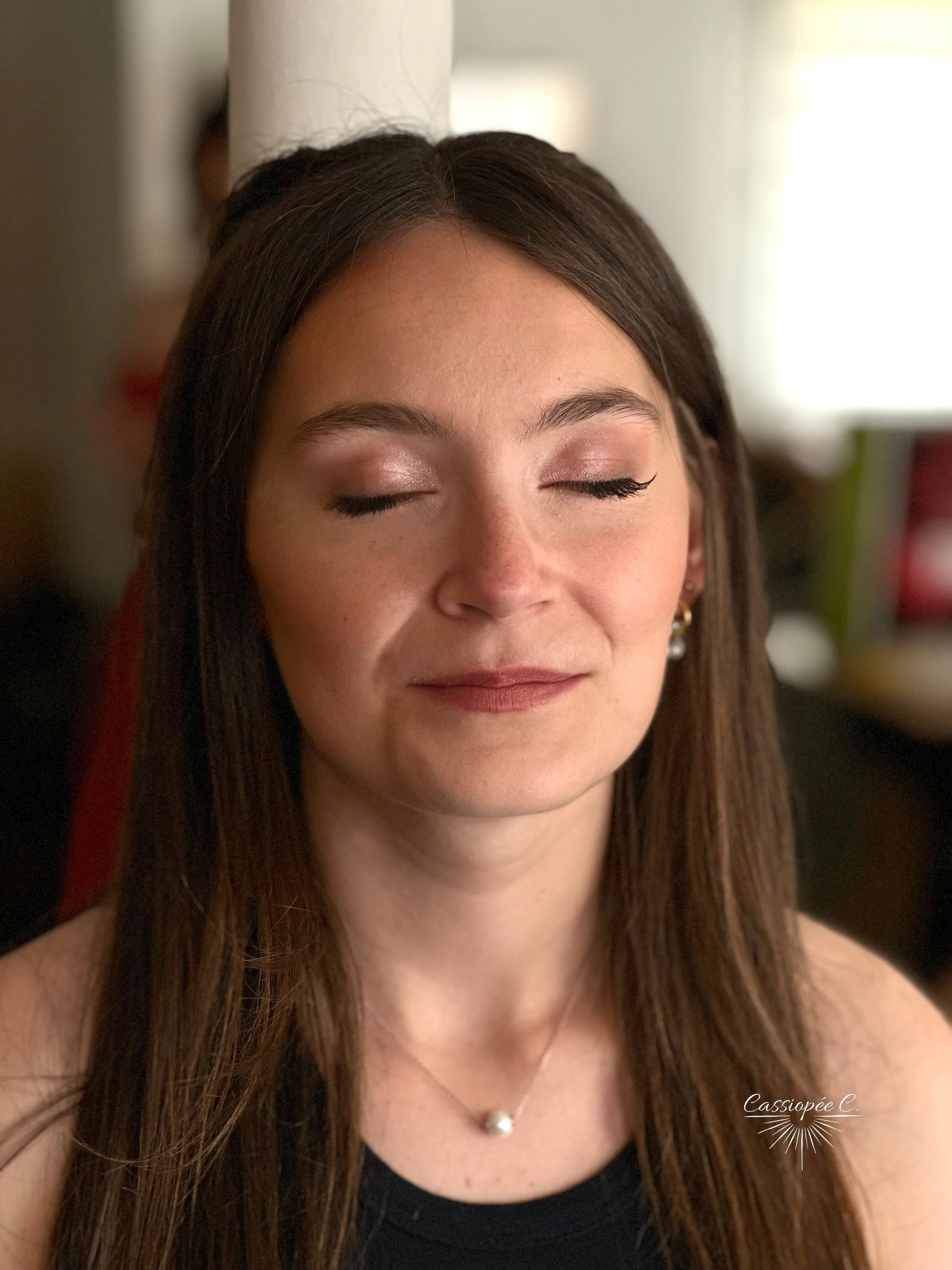 Jeune femme avec les cheveux longs, yeux bleus, souriant légèrement, dans un intérieur lumineux avec un maquillage pour un mariage.