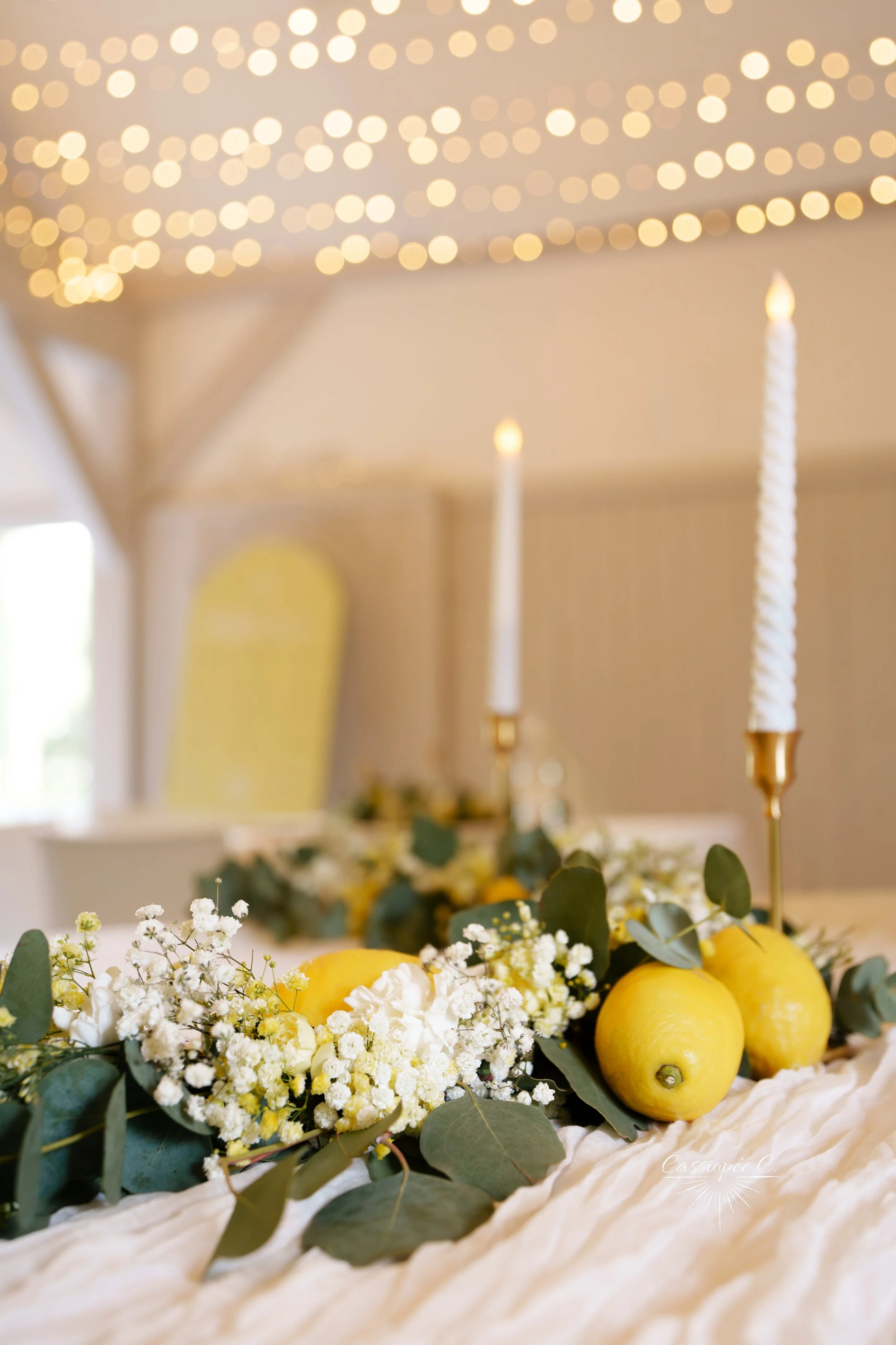 Décoration de table avec des citrons, des fleurs blanches et des bougies torsadées en chandeliers en métal, ambiance lumineuse chaleureuse.
