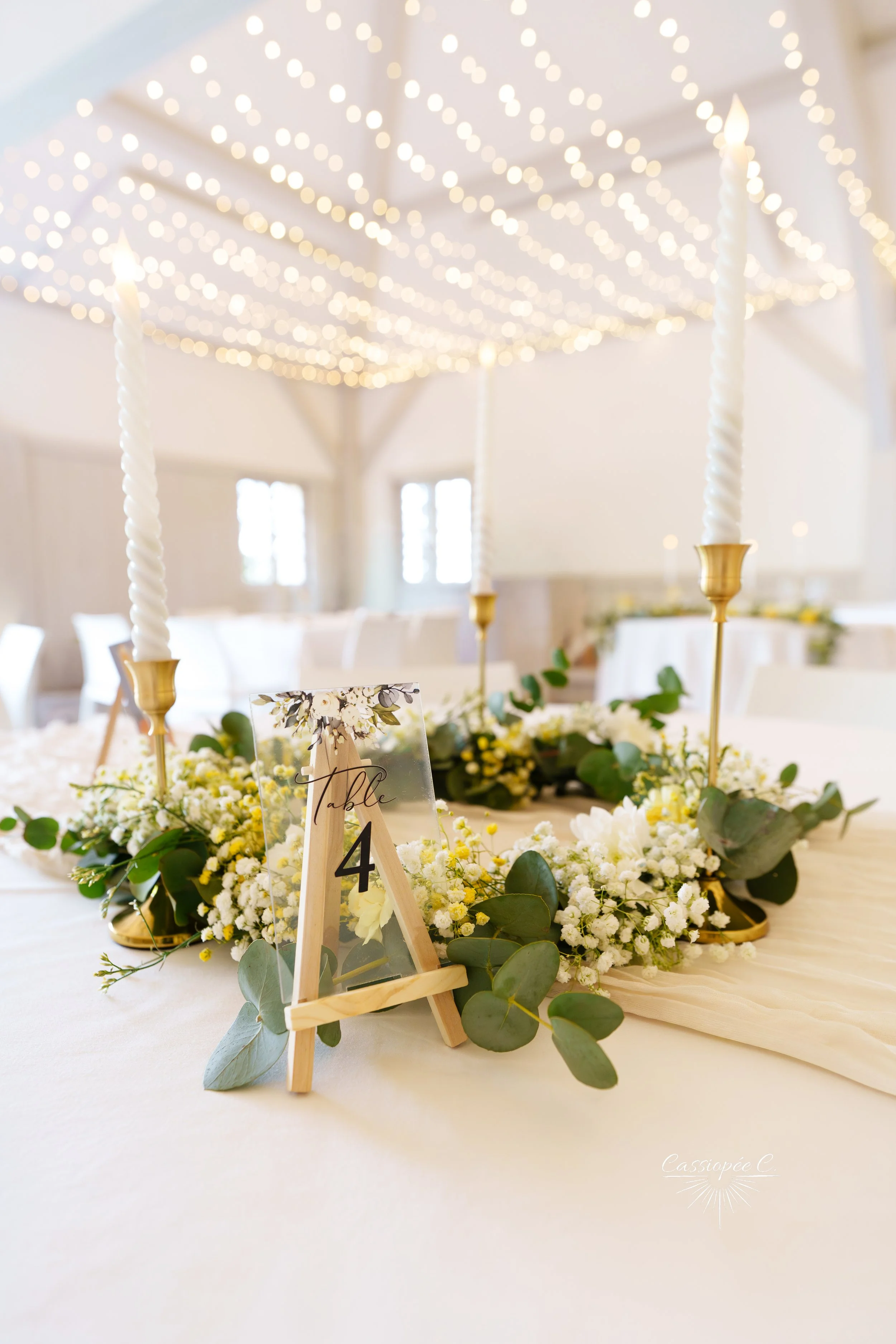 Centre de table de mariage avec bougies, fleurs blanches et feuillage vert, ambiance lumineuse et décorative pour un mariage. 