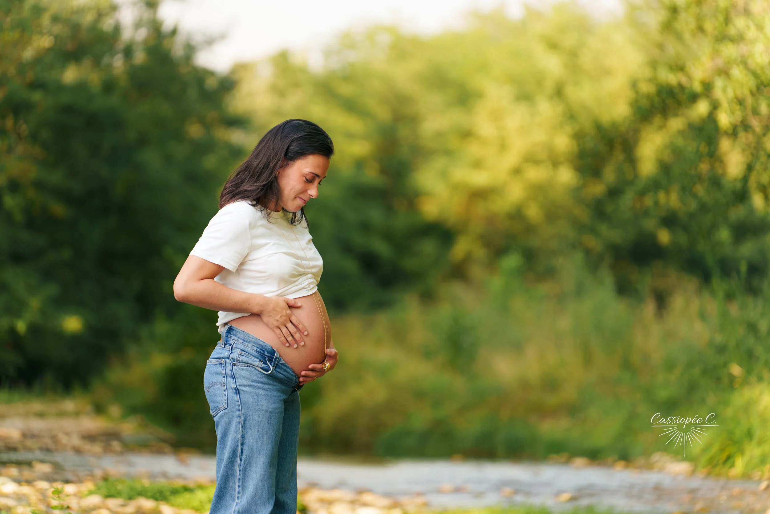 Femme enceinte regardant son ventre dans un parc verdoyant en plein air.