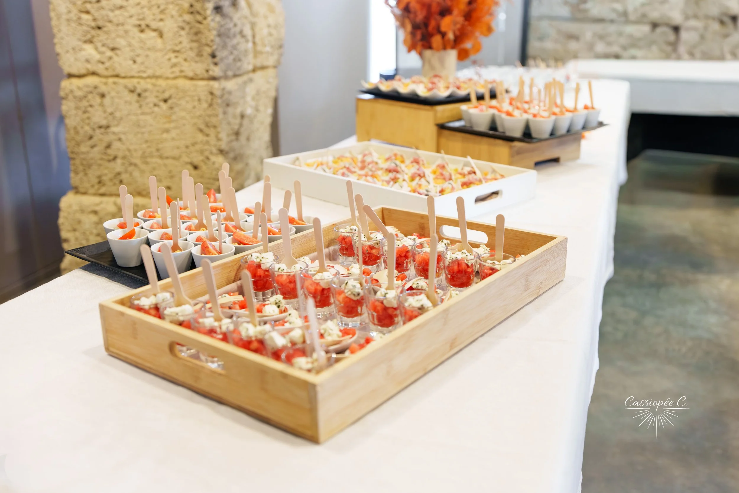Plateau avec des verrines et des petits fours, décoré avec un bouquet orangé dans une salle de réception.