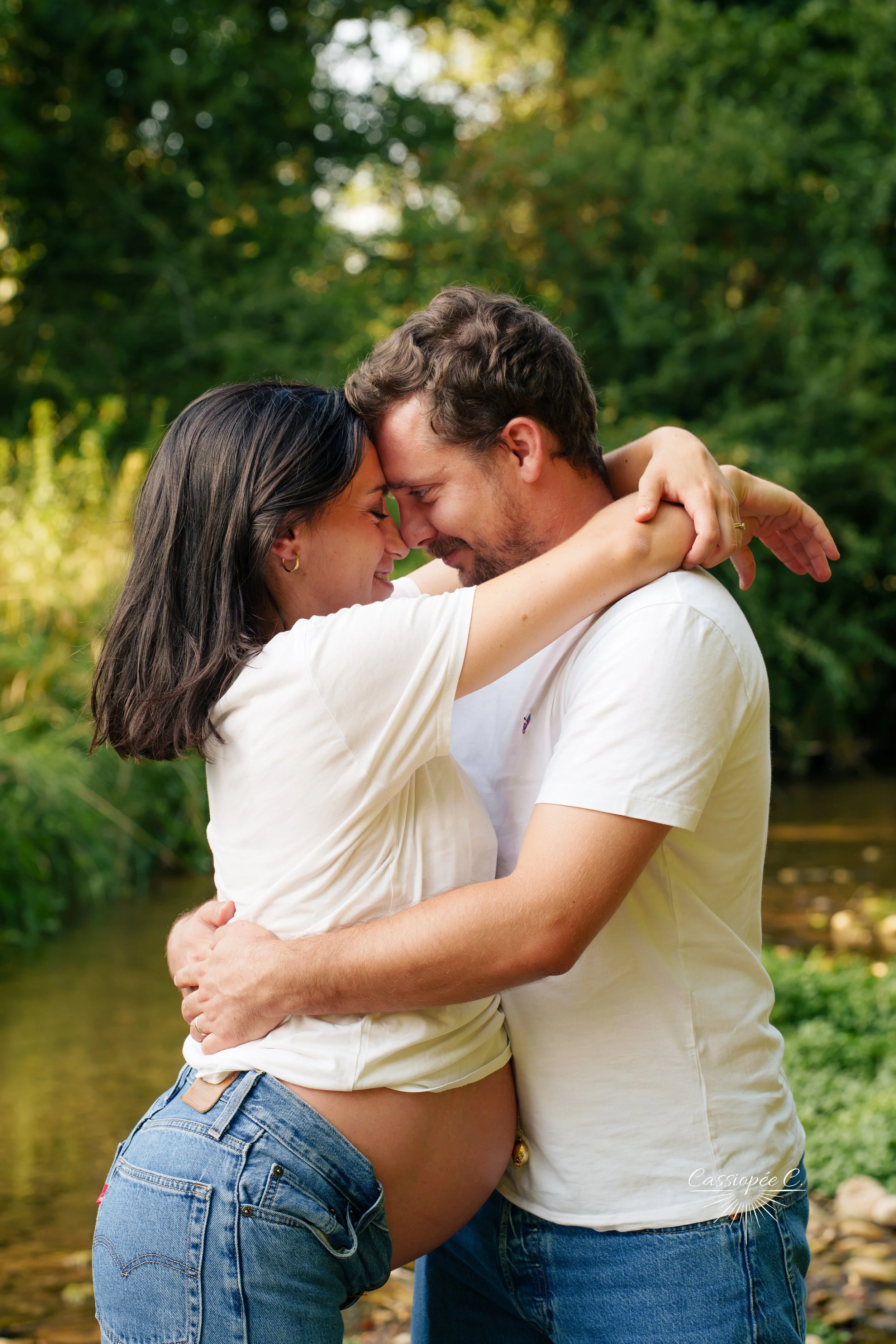 Un couple s'embrasse avec la tête contre la tête dans un lieu naturel verdoyant près de l'eau.