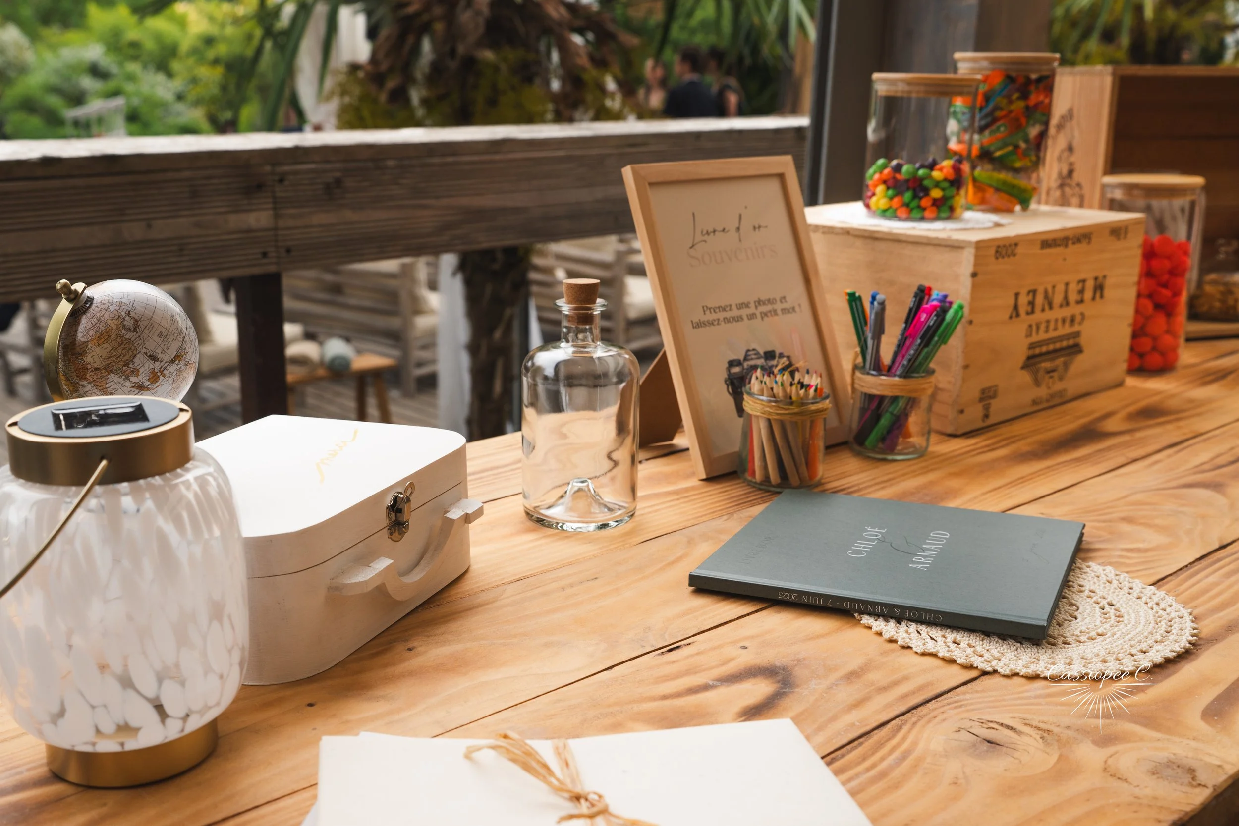 Coin d'une table en bois avec un globe miniatura, un coffre blanc, une bouteille en verre, une affiche encadrée, des crayons de couleur, une planchette en crochet, et des bocaux contenant des bonbons colorés, dans un espace décoré de manière chaleure