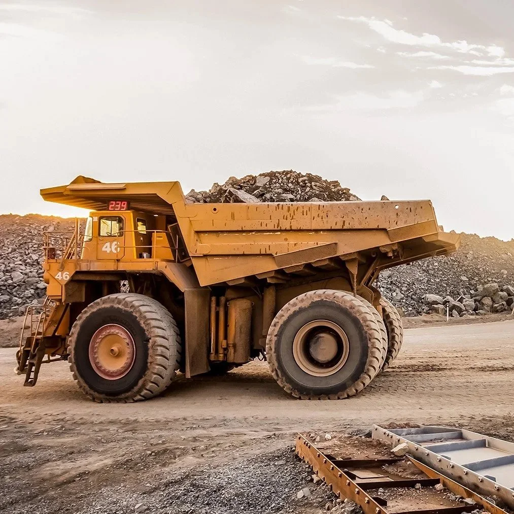 A large yellow dump truck filled with rocks at a mining or construction site during sunset.