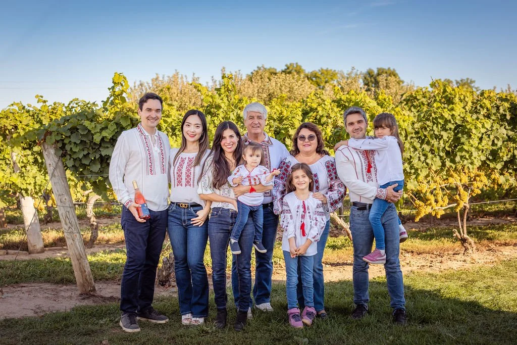 Dandor family of nine dressed in traditional Moldovan embroidered clothing standing in a vineyard during daytime.