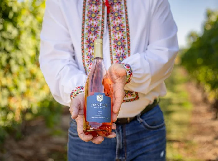 Person in traditional embroidered Moldovan shirt holding a bottle of rosé wine outdoors in Niagara-on-the-Lake on a sunny day.