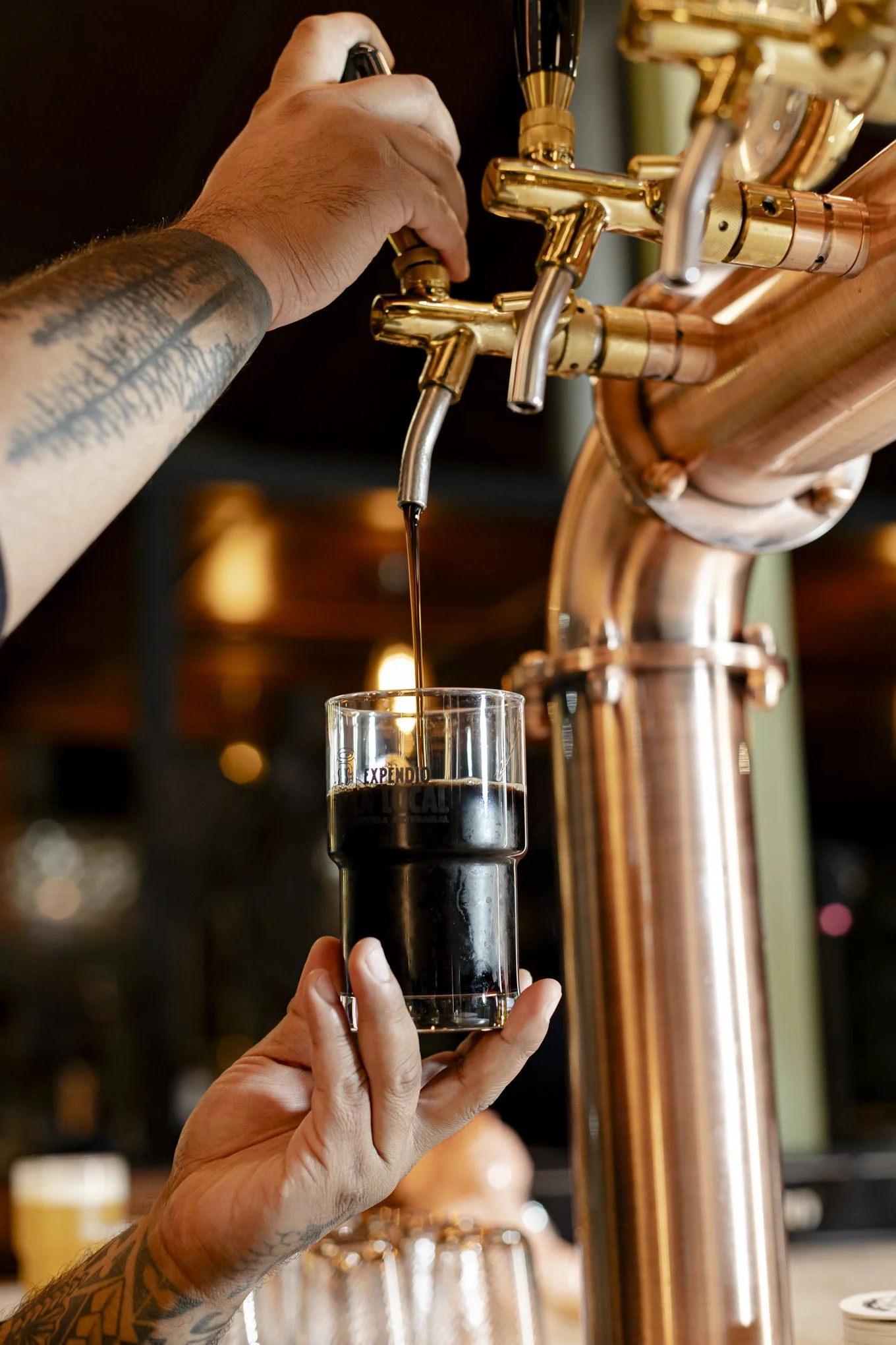 Una mano vertiendo cerveza oscura de una llave de caño de cobre en un vaso.