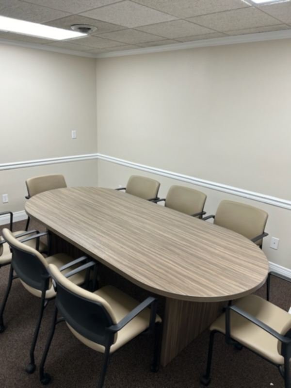 Empty conference room with a large wooden table and eight beige chairs.