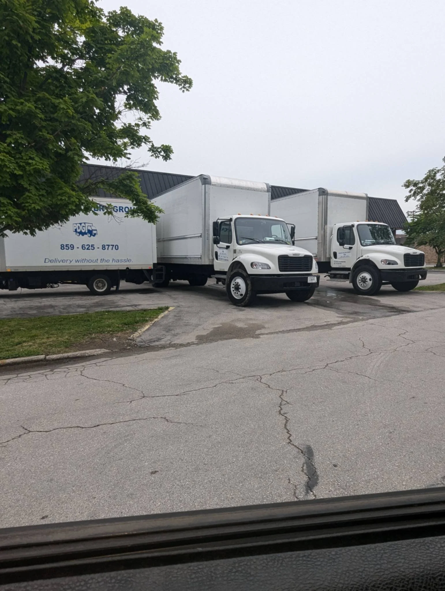Three delivery trucks parked on a street with a cloudy sky and a tree in the background.