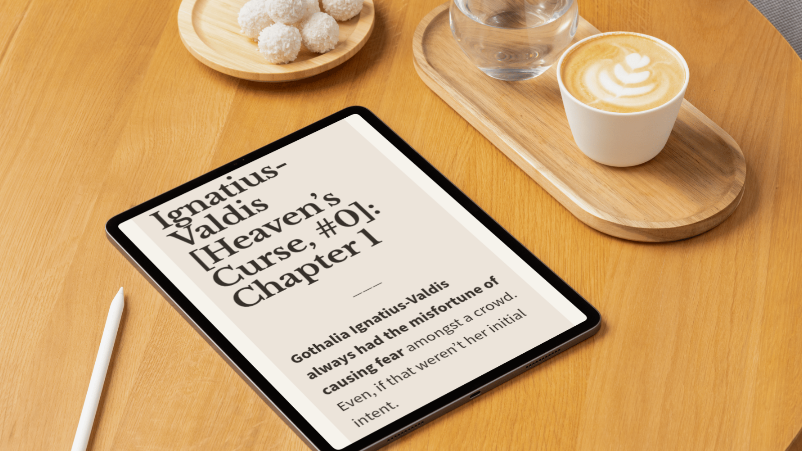 An iPad displays a book titled 'Ignatius-Valdis Heaven's Curse, #01: Chapter 1'. The tablet is on a wooden table next to a white stylus, a wooden tray with a glass of water and a cup of coffee with latte art, and a small plate of coconut-covered trea