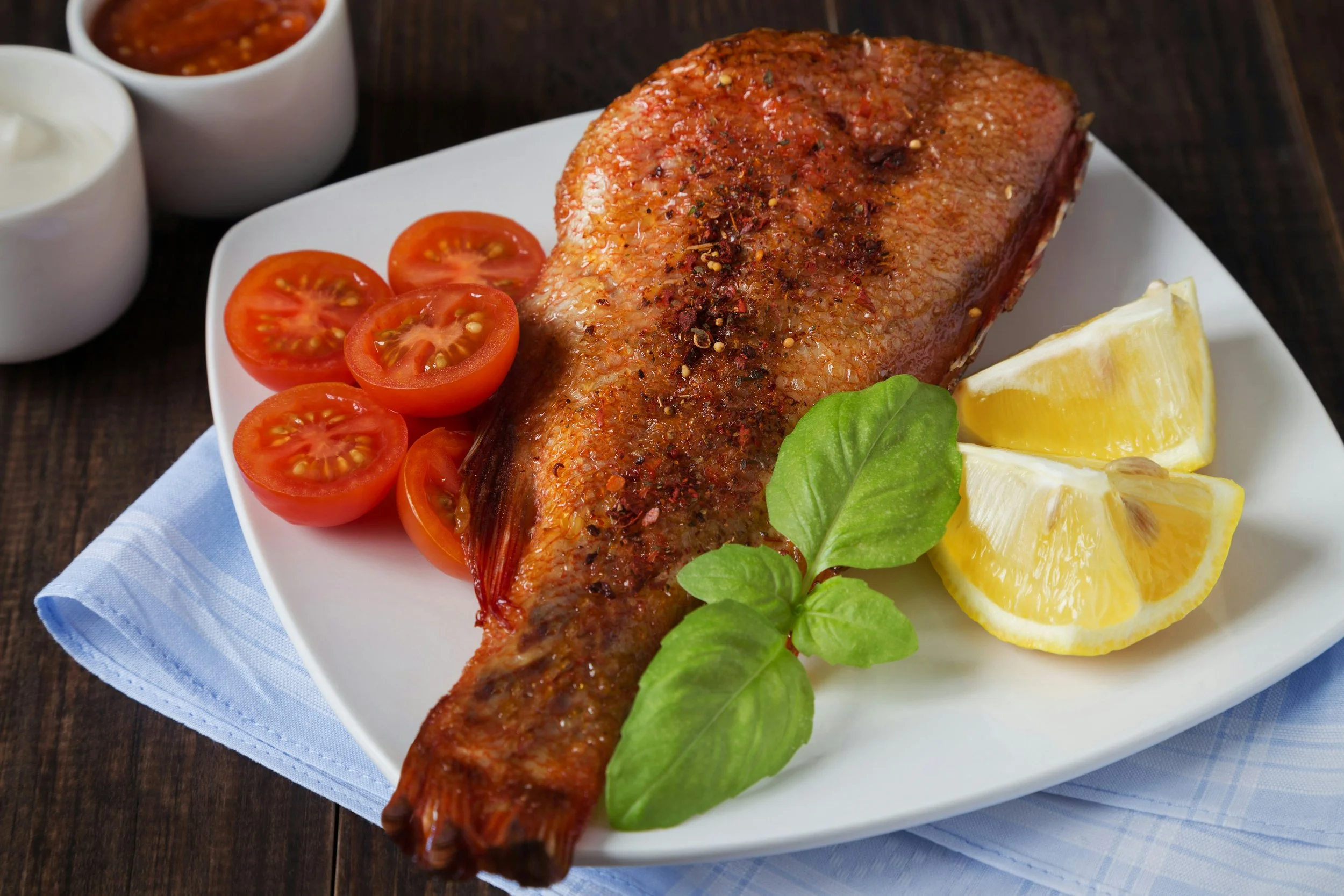 Poisson frit avec tomates cerises, tranches de citron, basilic, en sauce tomate et yaourt