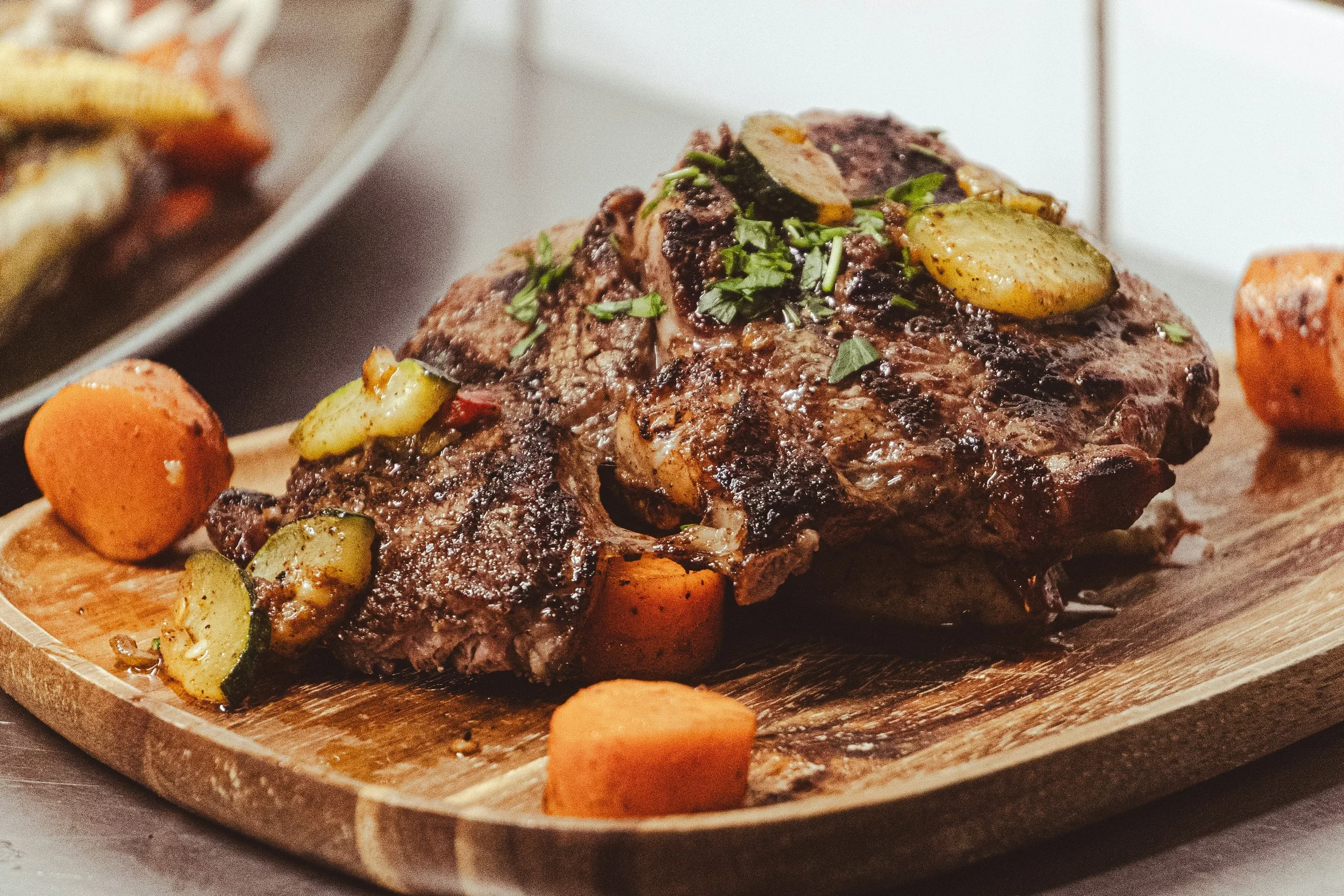 Une pièce de viande cuite avec des légumes, notamment des carottes et des courgettes, servie sur une planche en bois.
