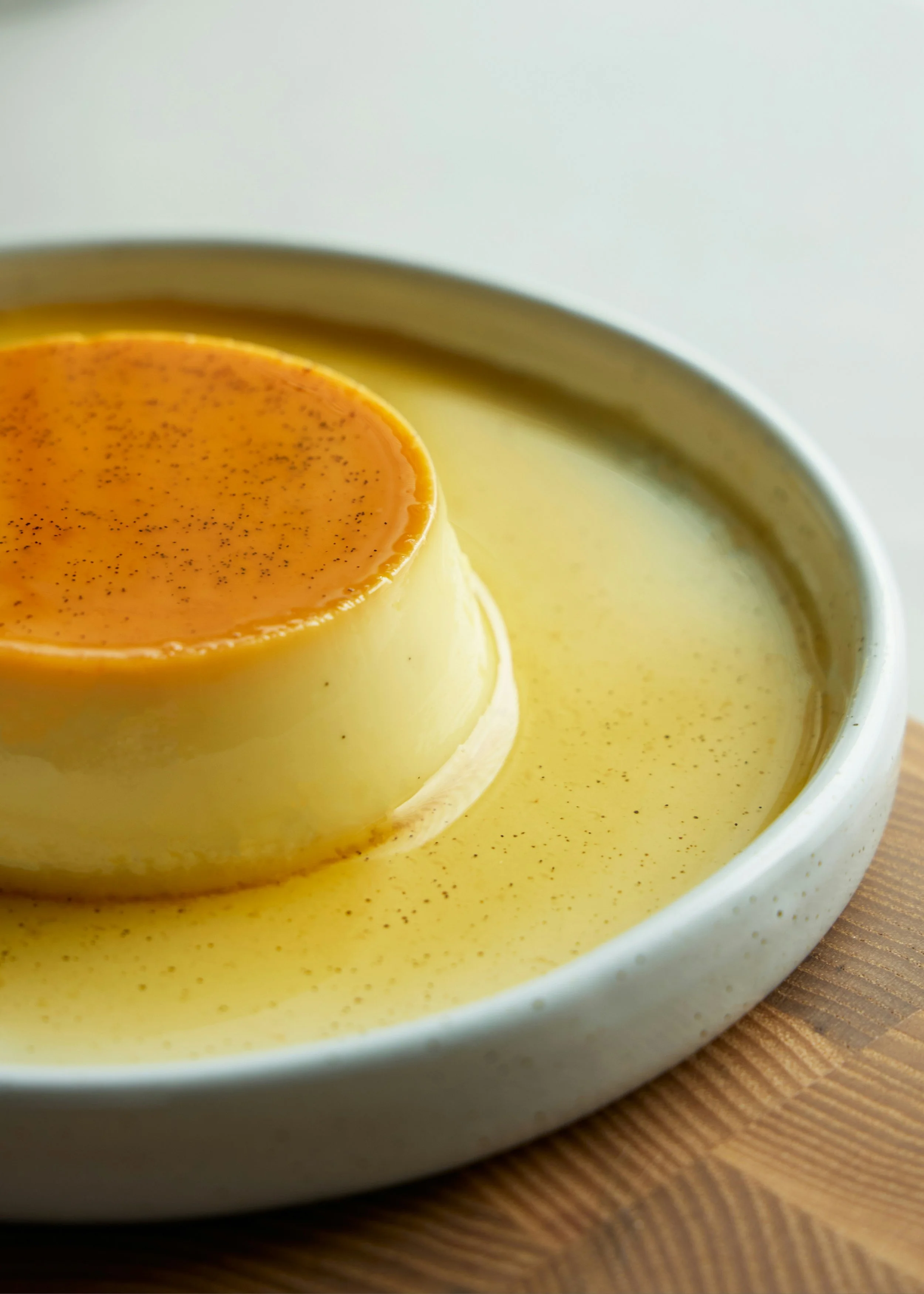 Crème caramel dans un bol blanc, avec une couche caramel au dessus, sur une surface en bois.