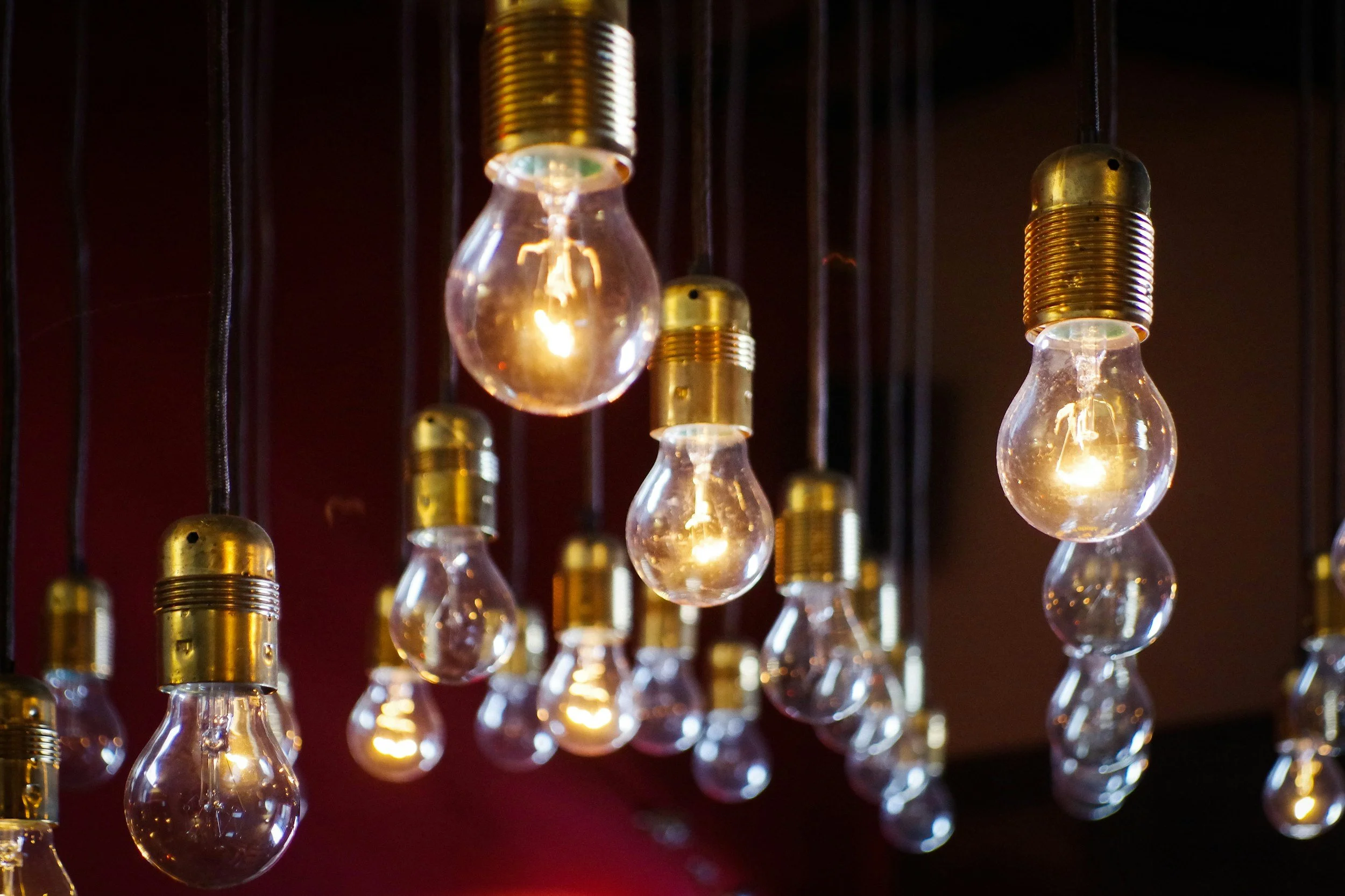 Multiple hanging light bulbs with illuminated filaments and gold-colored sockets against a dark background.
