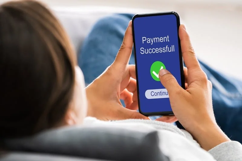 Person holding a smartphone makinga payment and getting a Payment Successful and a green checkmark when complete.
