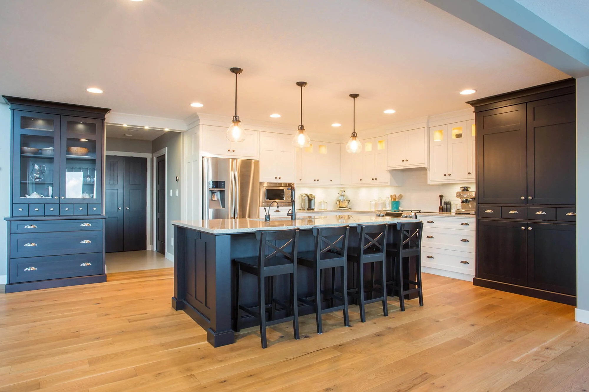 Modern kitchen with white and black cabinets, granite island with seating, stainless steel appliances, and pendant lighting.