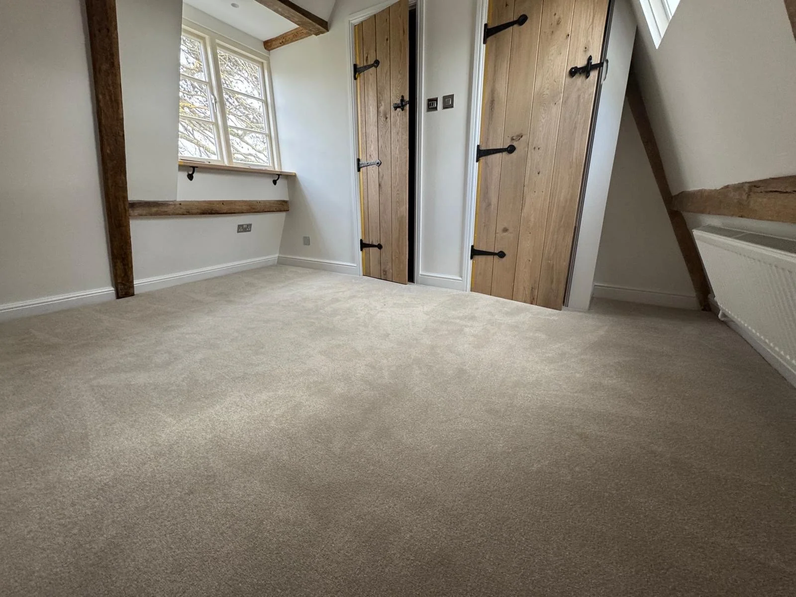 Empty room with beige carpet, white walls, a window with wooden trim, rustic wooden sliding closet doors, and wooden beams on the ceiling.