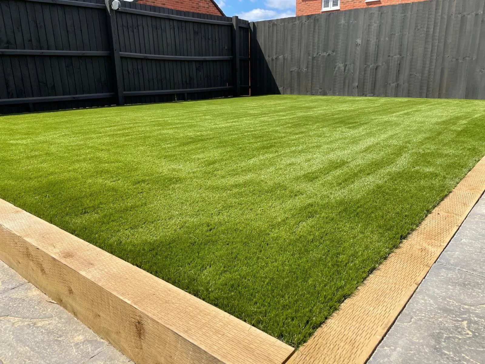 A freshly laid sod lawn enclosed by a wooden border with a black fence in the background.