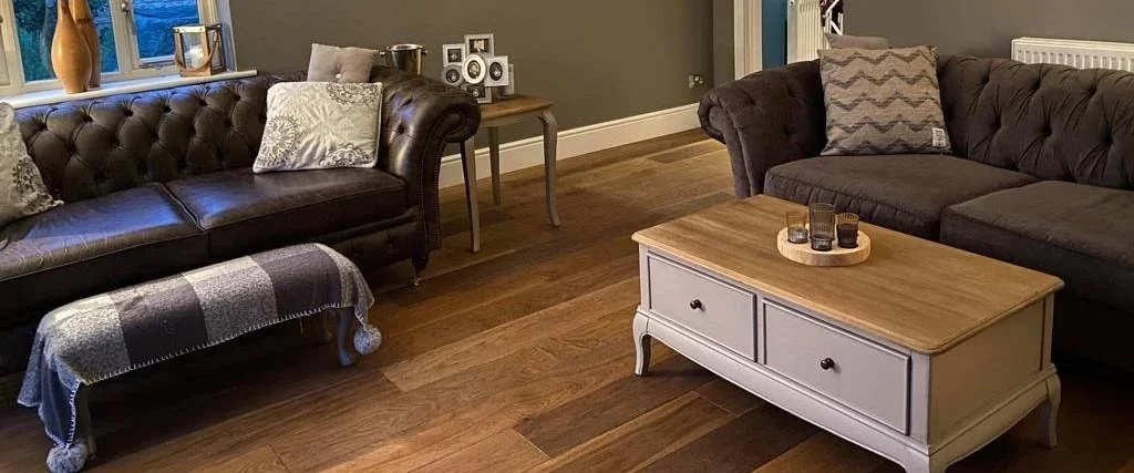 Living room with two brown sofas, decorative cushions, a wooden coffee table with drawers, and a window with a windowsill decorated with vases and picture frames.