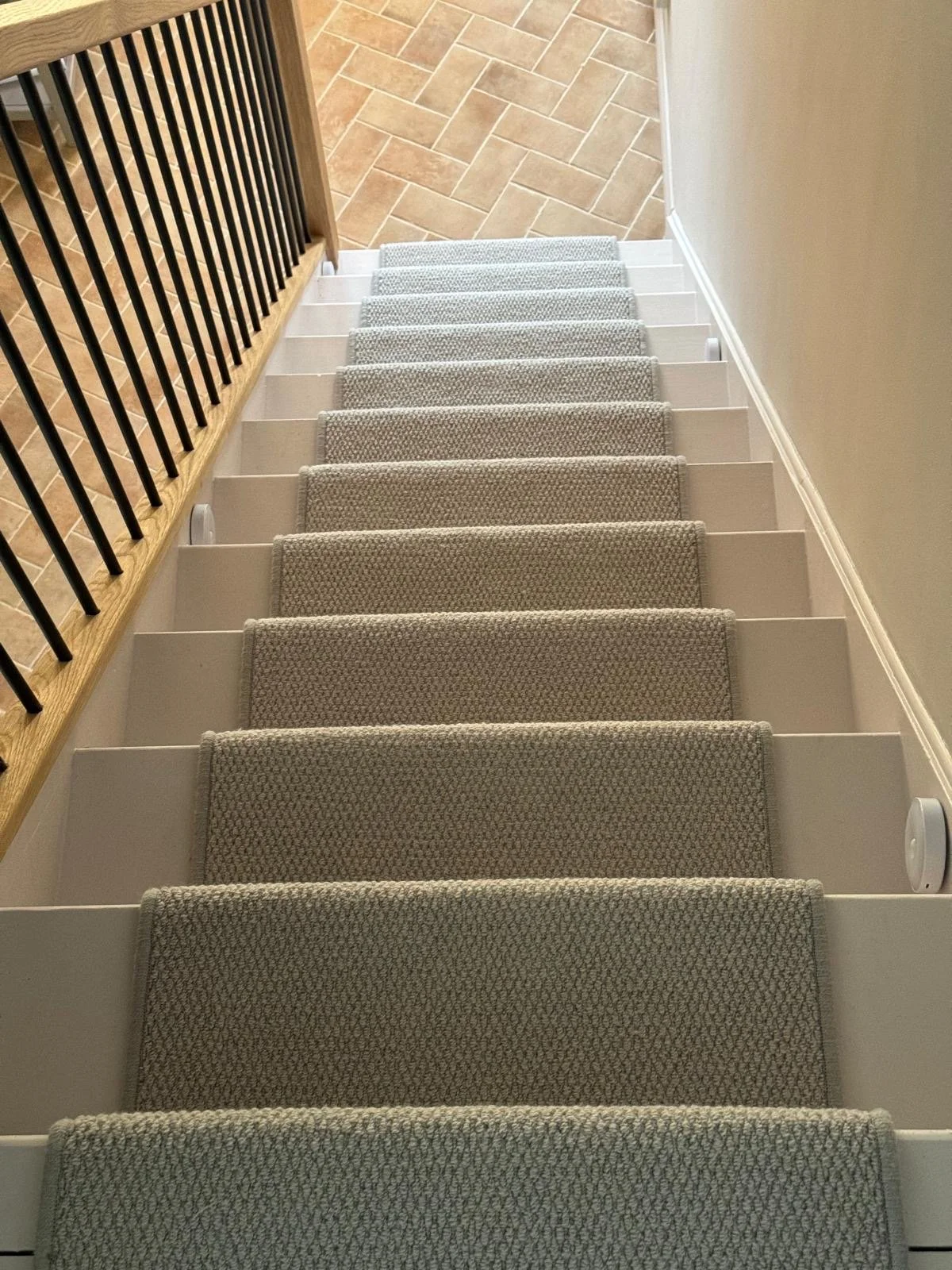 Overhead view of carpeted stairs with handrail on the left and a wall on the right, leading down to a tiled floor.