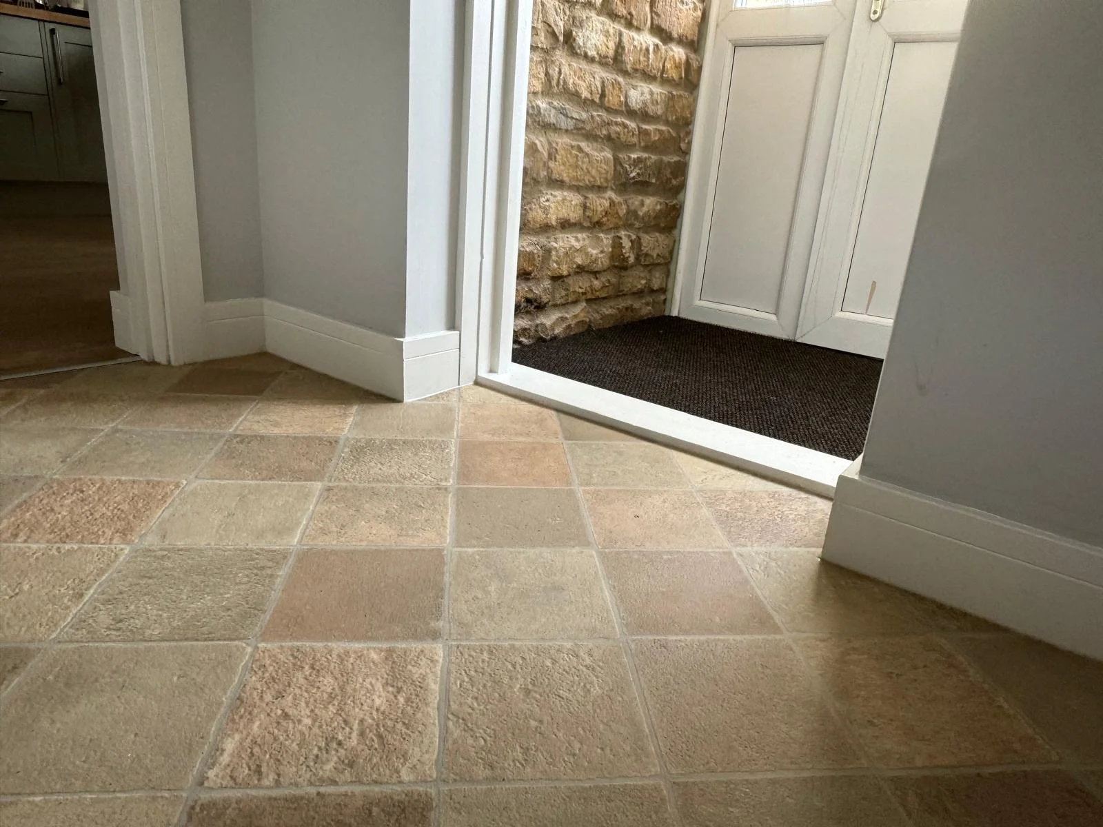 Close-up of tiled floor at doorway with a black mat, white door, and brick wall inside the house.