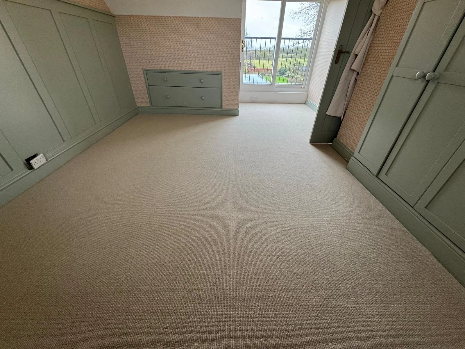 Empty room with green built-in cabinets, beige carpet, and a balcony door with view of outdoor garden.