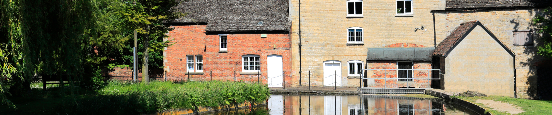 A row of old buildings with brick and stone facades next to a waterway, with reflections visible in the water.