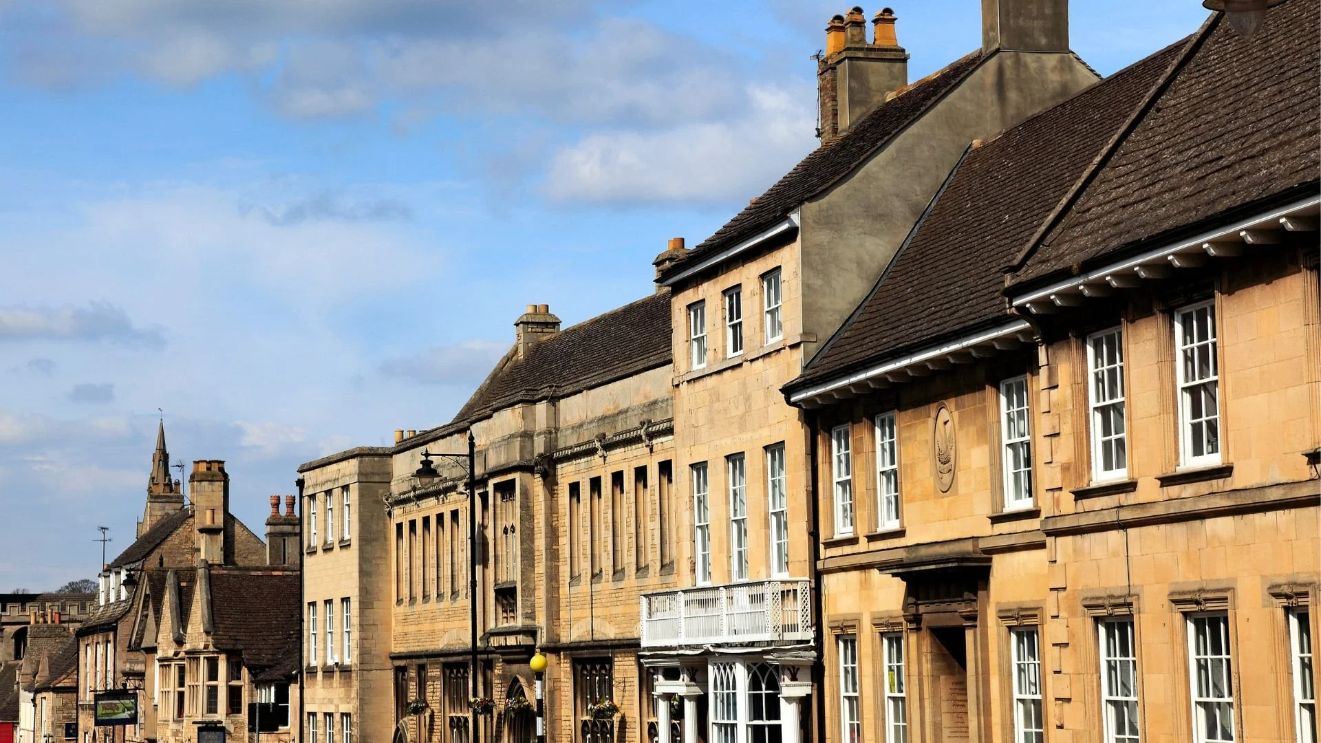 A row of historic buildings with stone facades and pitched roofs, under a partly cloudy sky.
