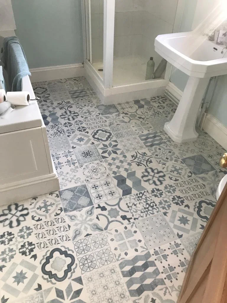 Bathroom with patterned tile floor, white sink, glass shower enclosure, and toilet with toilet paper rolls.