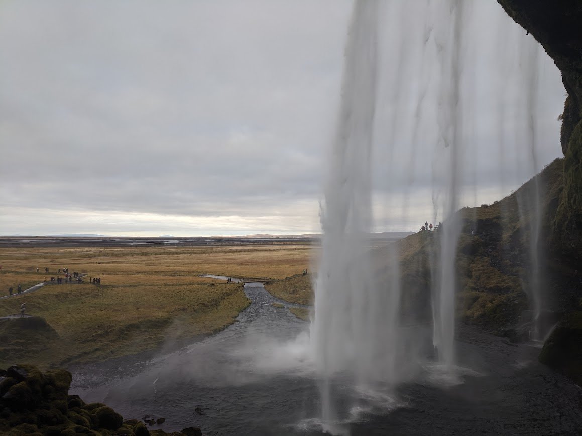 View of Skogafoss waterfall in Iceland, with mist created by falling water and a misty landscape in the background.