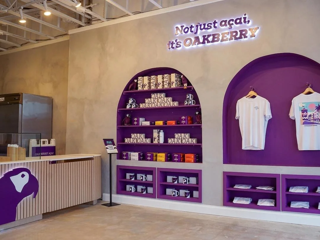 Interior of a store with purple shelves displaying products, T-shirts on hangers, and a sign saying "Not just açai, it's OAKBERRY"