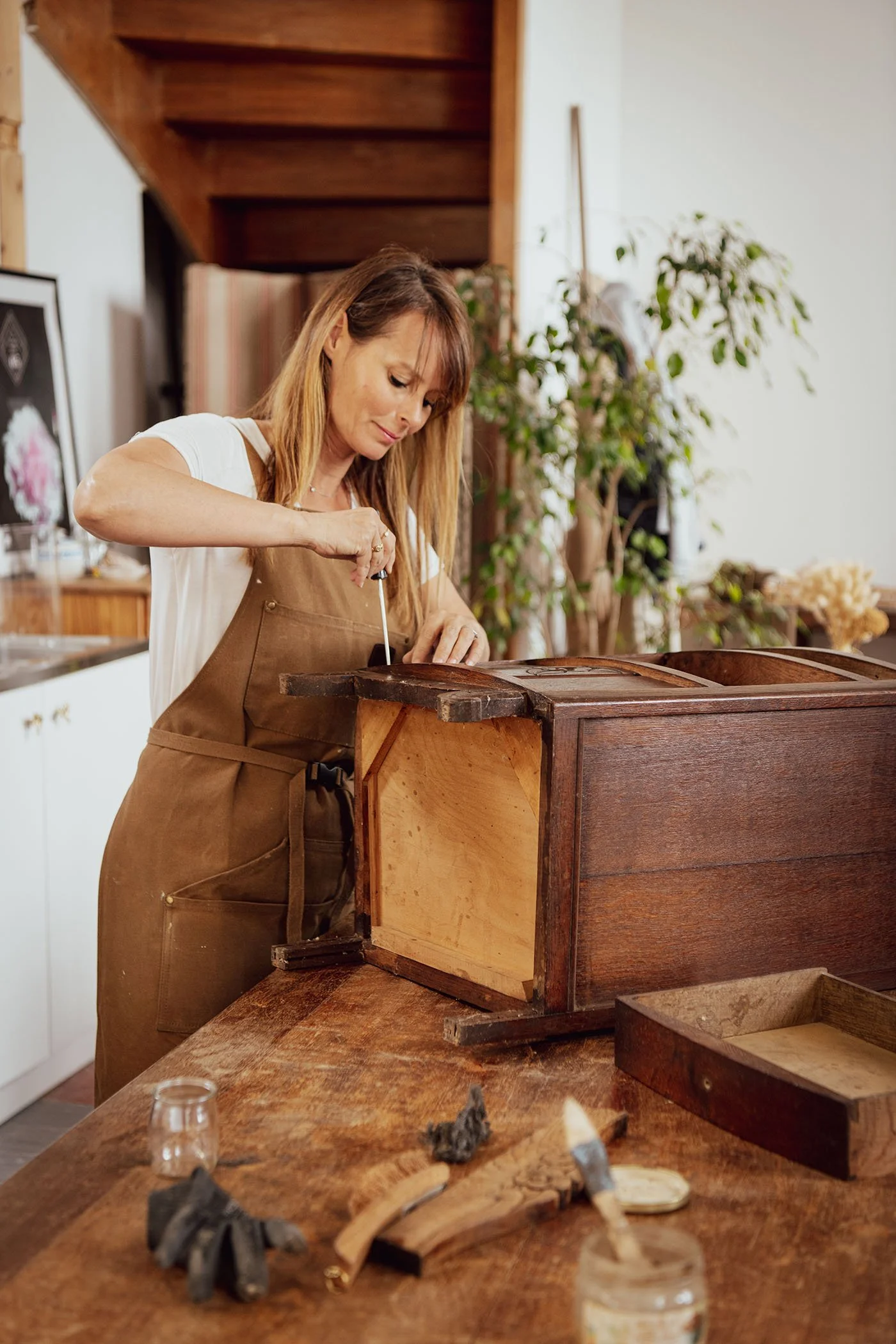 Amélie en train de restaurer une ancienne commode dans son atelier, serrant une pièce en bois avec précision. Travail artisanal et savoir-faire Meliwood.