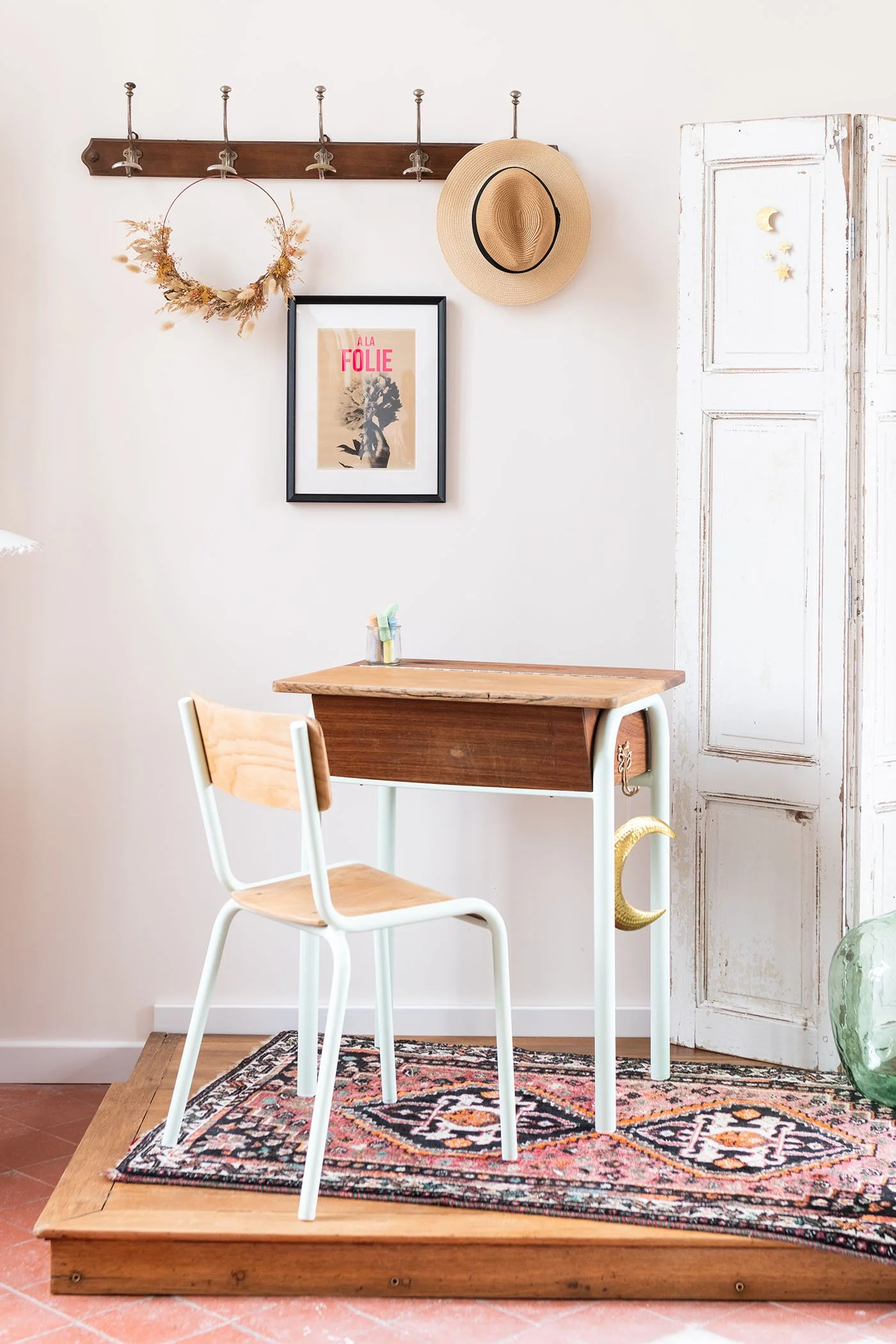 Bureau d’écolier vintage restauré mis en scène avec paravent patiné, dame-jeanne verte et affiche rétro dans l’univers Meliwood.